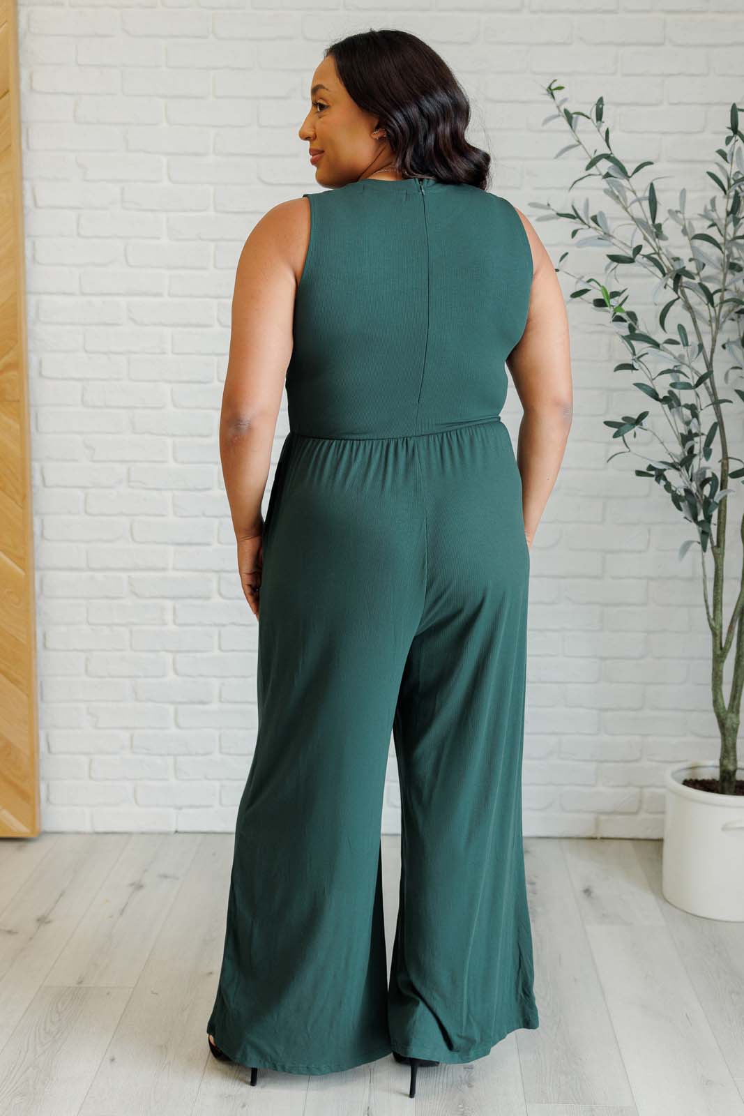 Green ribbed wide-leg jumpsuit with round neckline, sleeveless design, flattering stretchy waistline, hidden zipper closure, and pockets. Offers full bra coverage with wide straps.