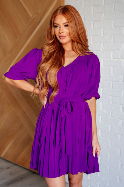Front view of Hoda Pleated Chiffon Dress with button-up V-neckline, puff sleeves, self-tie belt, and pleated chiffon skirt.