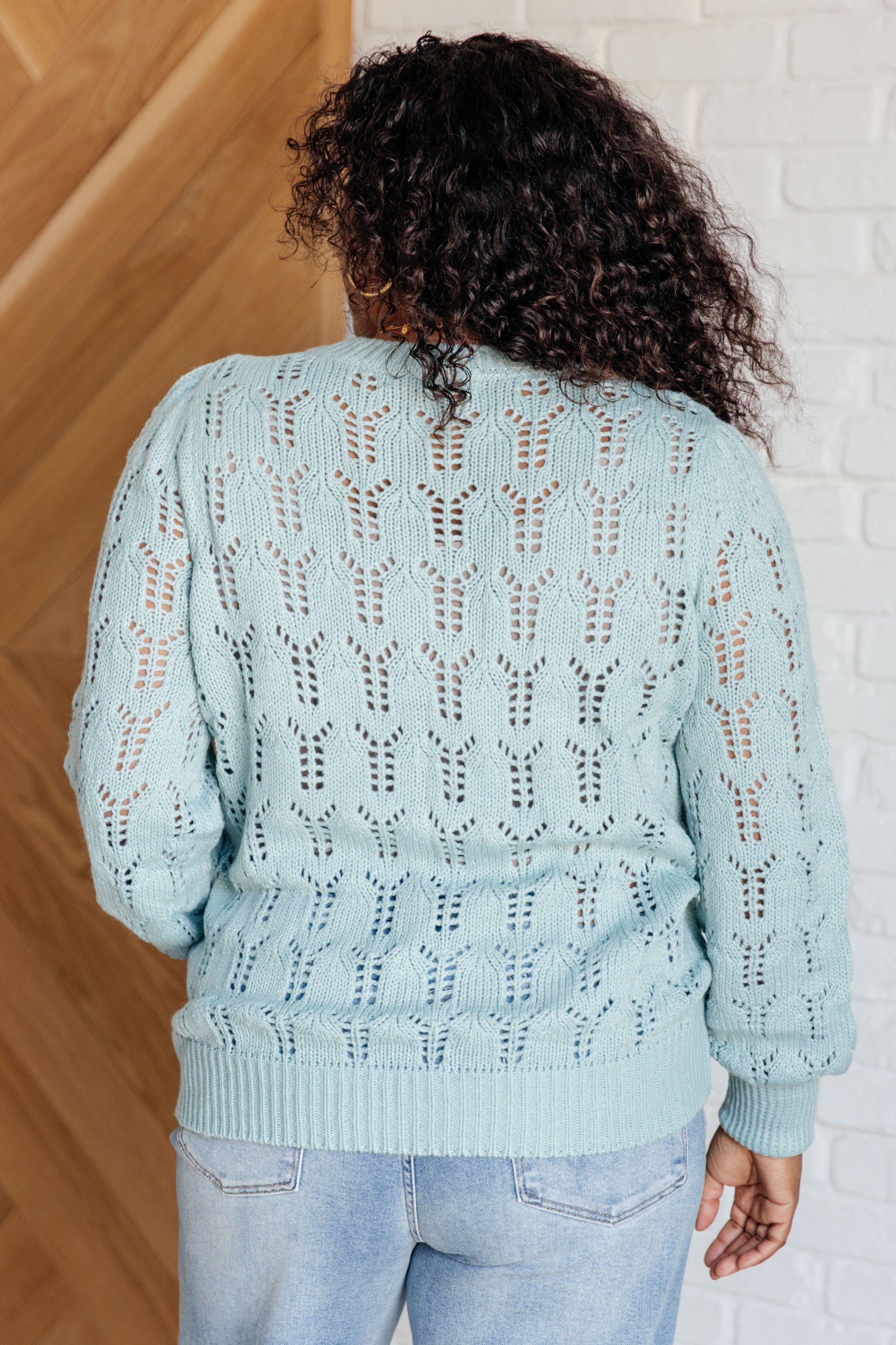 Light blue pointelle knit sweater with a round neckline, long cuffed sleeves, and sheer, lightweight fabric.