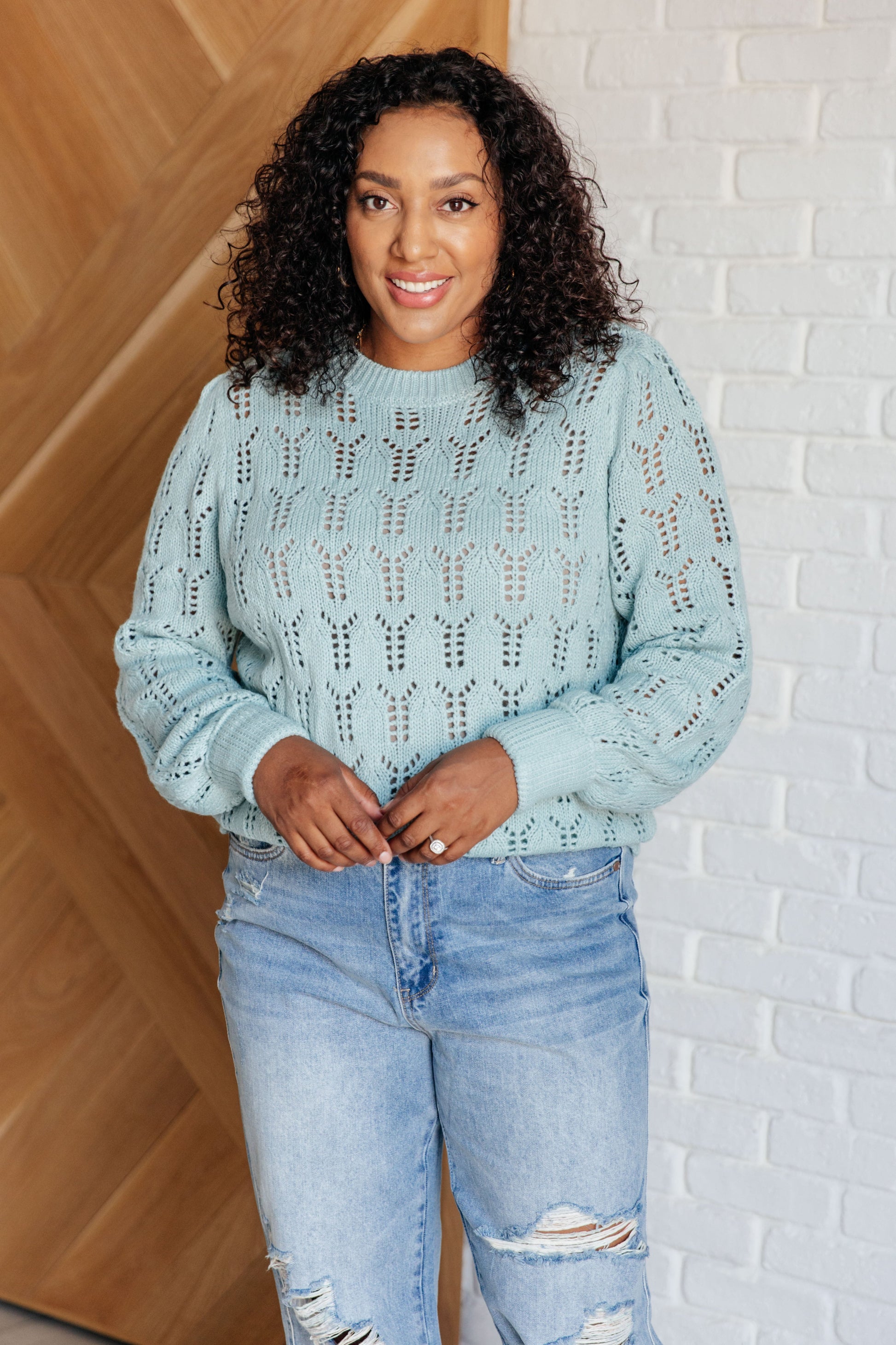 Light blue pointelle knit sweater with a round neckline, long cuffed sleeves, and sheer, lightweight fabric.