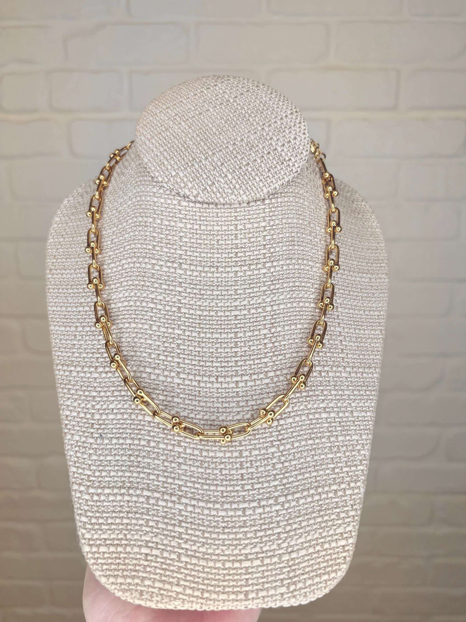 Large gold link necklace displayed on a jewelry stand, front view, showcasing its 18K gold-plated stainless steel finish and elegant design.