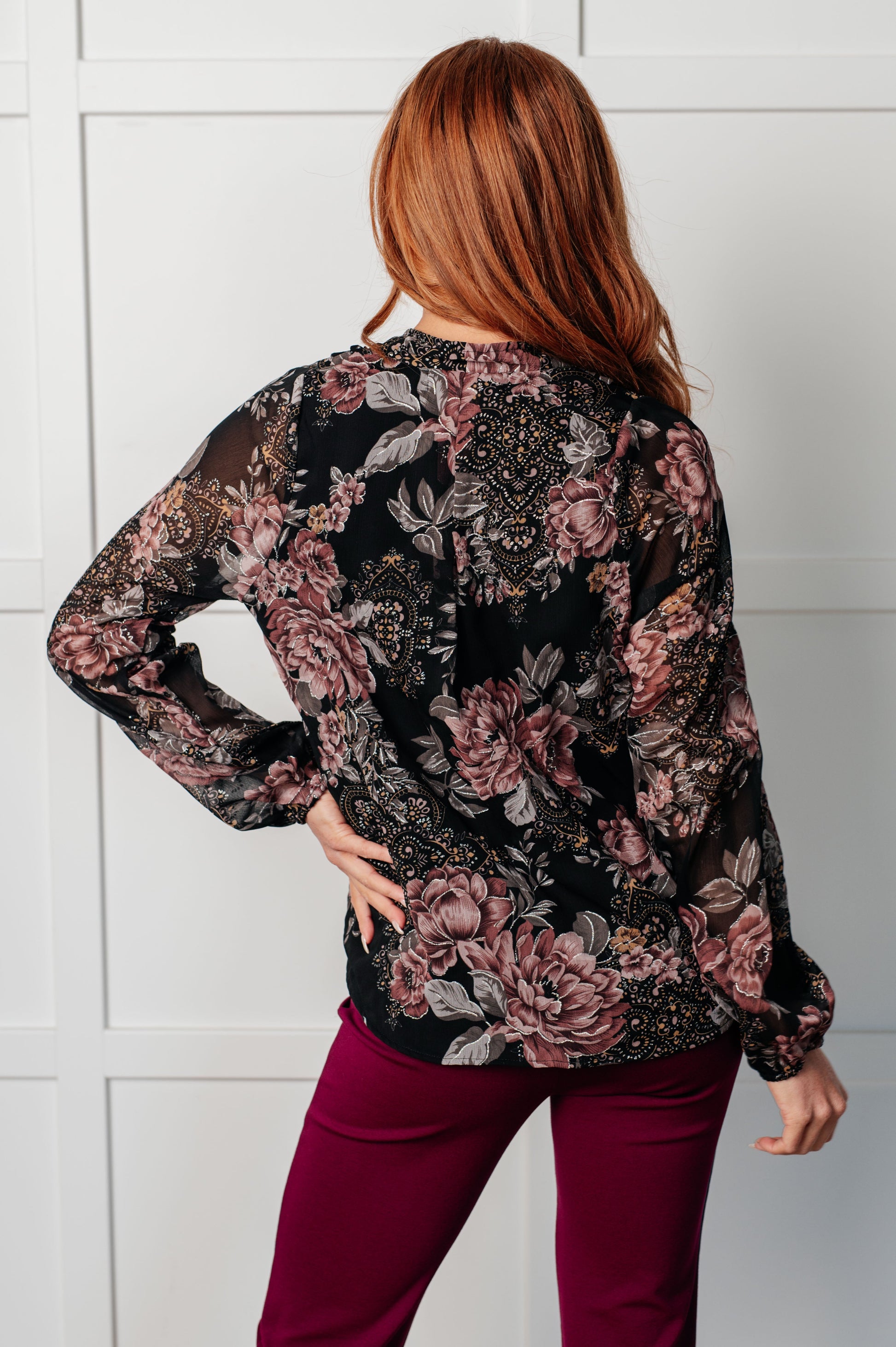 Women's surplice floral blouse in black chiffon with floral print, featuring a v-neckline, surplice bodice with hook and eye closure, long balloon sleeves with cased elastic cuffs, and scooped hemline with cased elastic front hemline. Lined bodice.