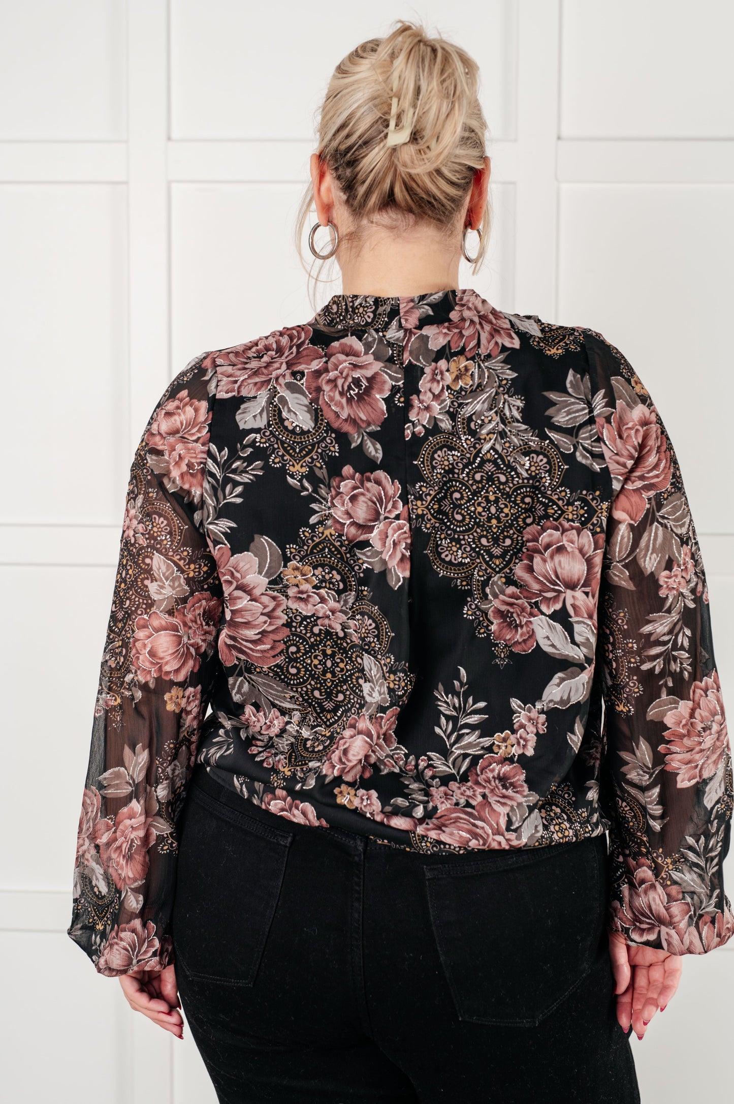 Back view of plus size women's surplice floral blouse in black chiffon with floral print, featuring a v-neckline, surplice bodice with hook and eye closure, long balloon sleeves with cased elastic cuffs, and scooped hemline with cased elastic front hemline. Lined bodice.