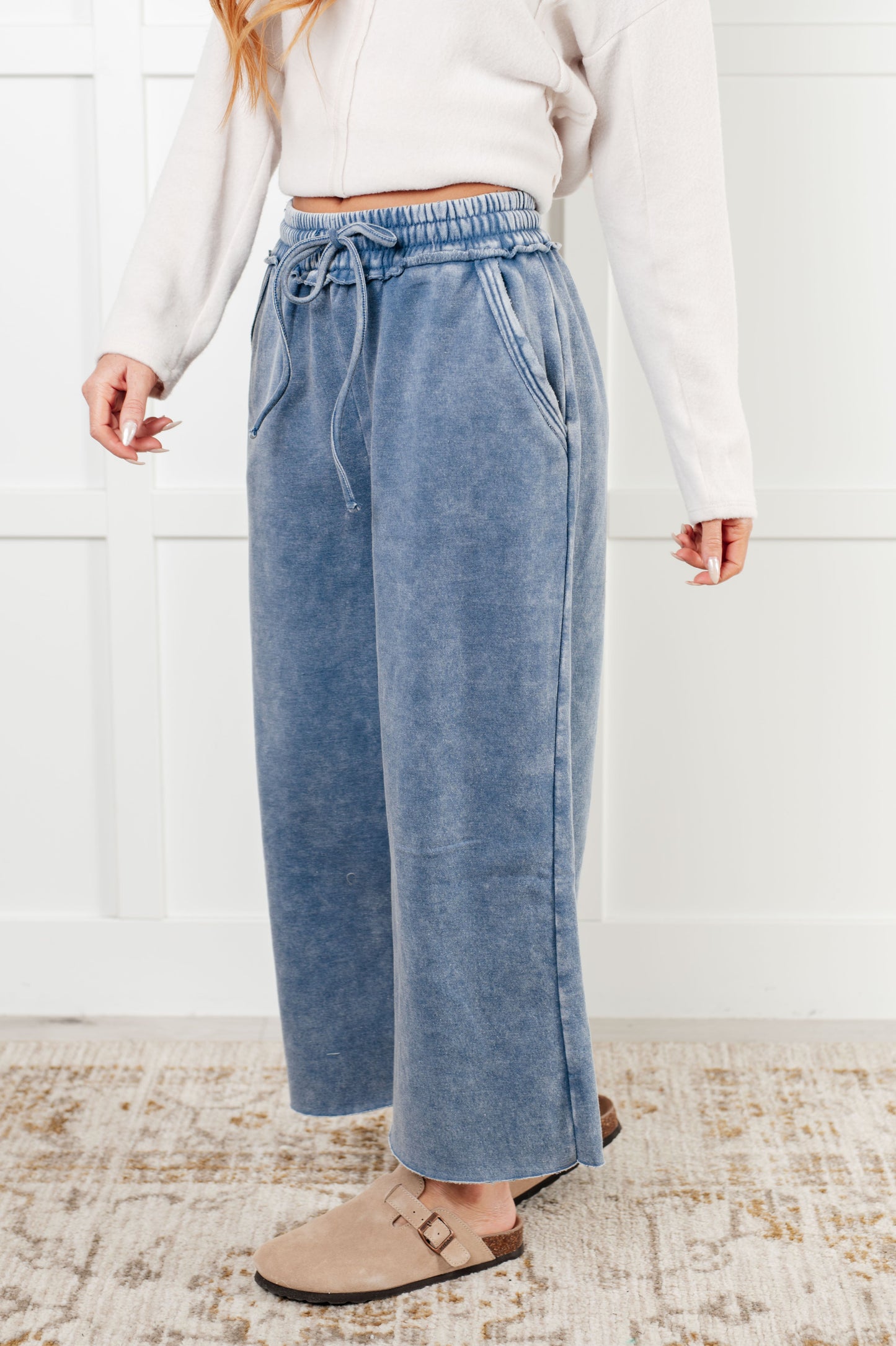 Indie Wide Leg Cropped Pants in soft fleece, featuring a trendy mineral wash in dusty blue. Designed with a drawstring elastic waist, functional side pockets, raw seam details, wide leg, and cropped length for a cozy, stylish, and relaxed look.