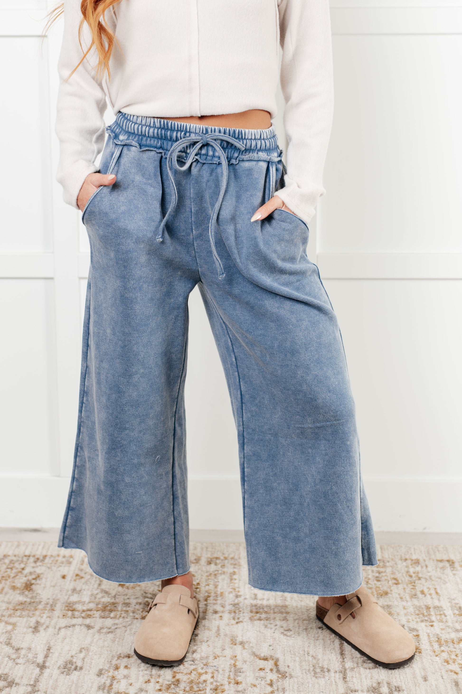 Indie Wide Leg Cropped Pants in soft fleece, featuring a trendy mineral wash in dusty blue. Designed with a drawstring elastic waist, functional side pockets, raw seam details, wide leg, and cropped length for a cozy, stylish, and relaxed look.