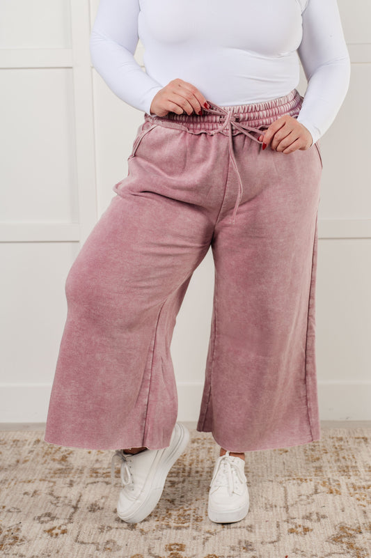 Indie Wide Leg Cropped Pants in soft fleece, featuring a trendy mineral wash in light rose. Designed with a drawstring elastic waist, functional side pockets, raw seam details, wide leg, and cropped length for a cozy, stylish, and relaxed look.