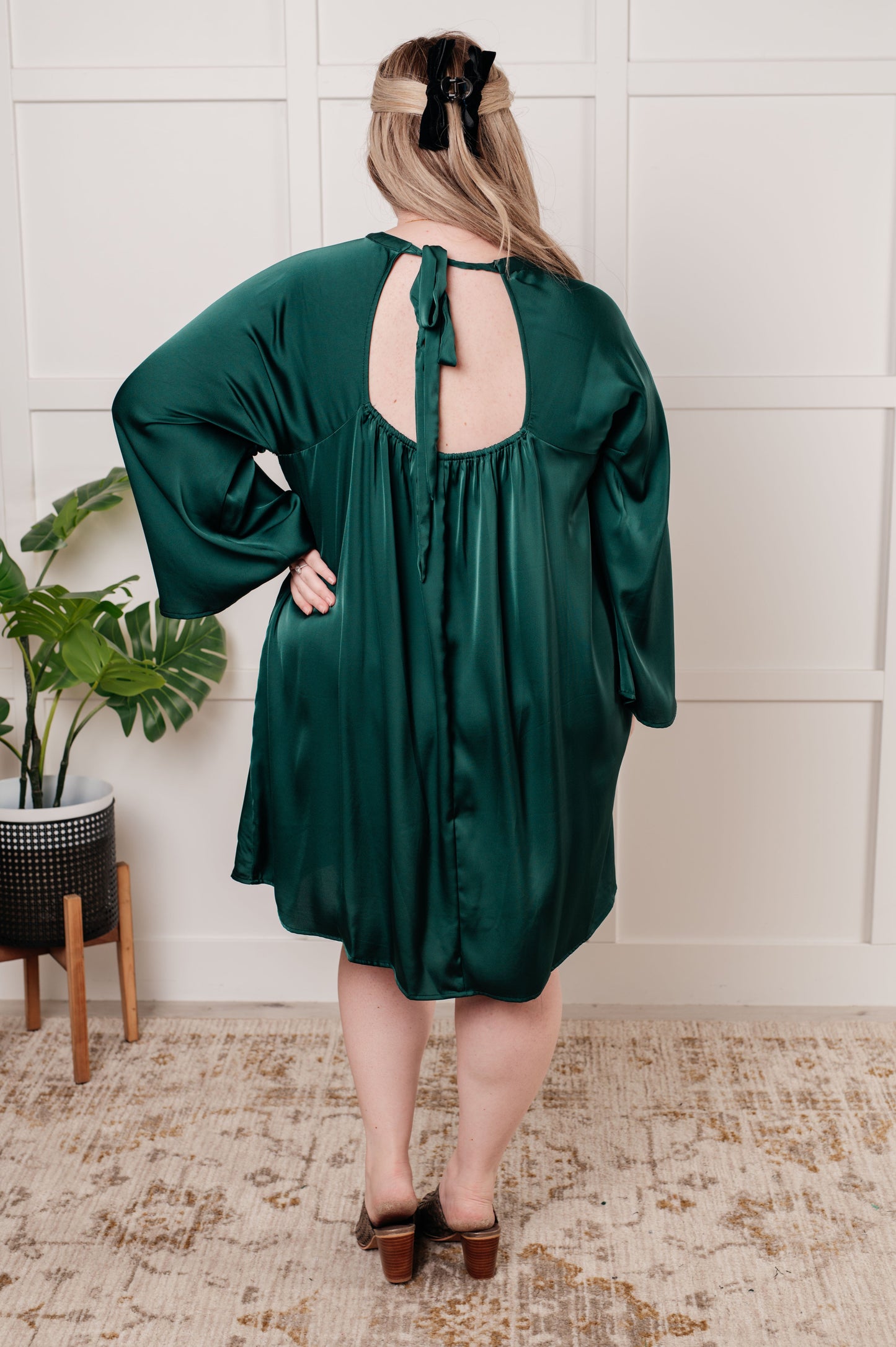 Emerald green poly satin A-line dress with banded mock neckline, long raglan bell sleeves, and back cased elastic for a flattering fit. Features a back cutout and tie closure. 