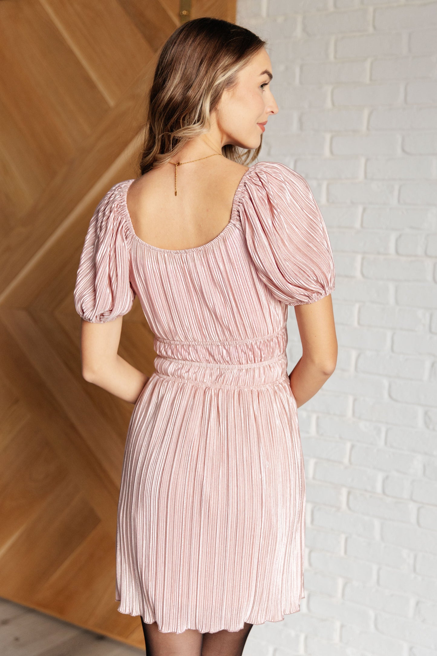 Pink poly satin plissé dress with a scoop neckline, off-shoulder option, short balloon sleeves, elastic cuffs, and a lined skirt.