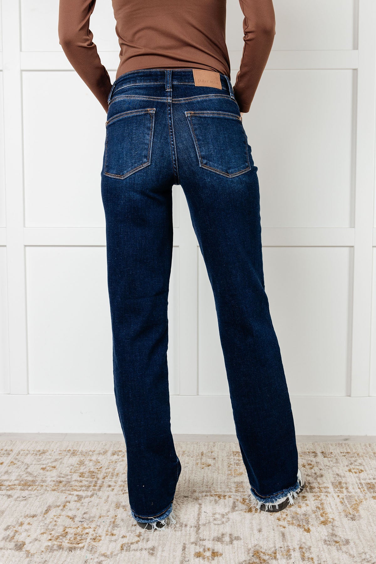 Back view of the Mid Rise Jean with dark wash, non-distressed design, straight-leg silhouette, and frayed hem.