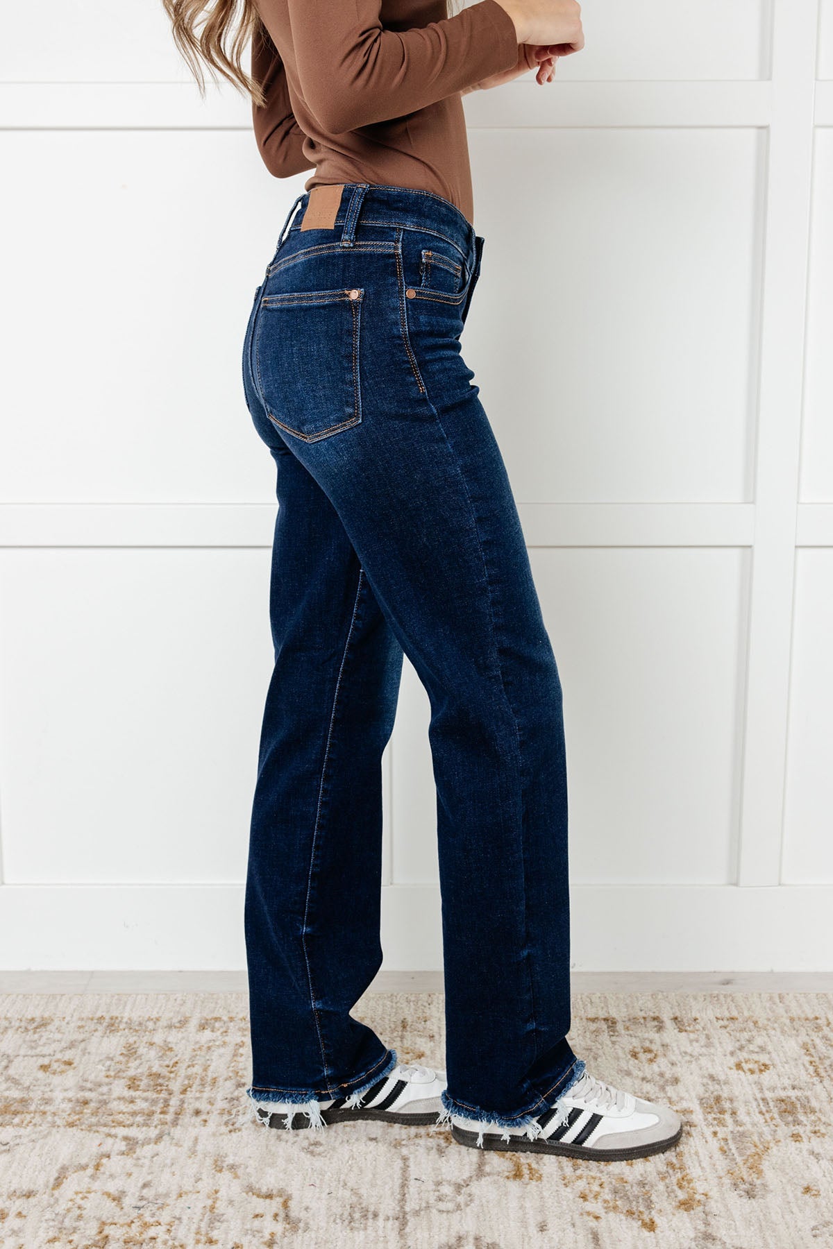 Side view of the Mid Rise Jean with dark wash, non-distressed design, straight-leg silhouette, and frayed hem.