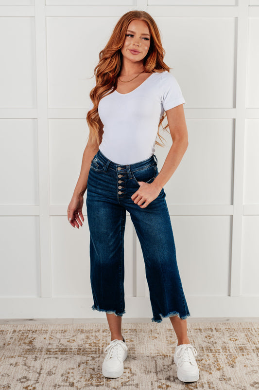 Janice High Rise Button Fly Wide Leg Crop Jeans by Judy Blue in a dark wash. Features a high-rise waist, button fly closure, wide leg crop silhouette, raw hem, and 4-way stretch for comfort and style. Perfect for a playful yet sophisticated look.