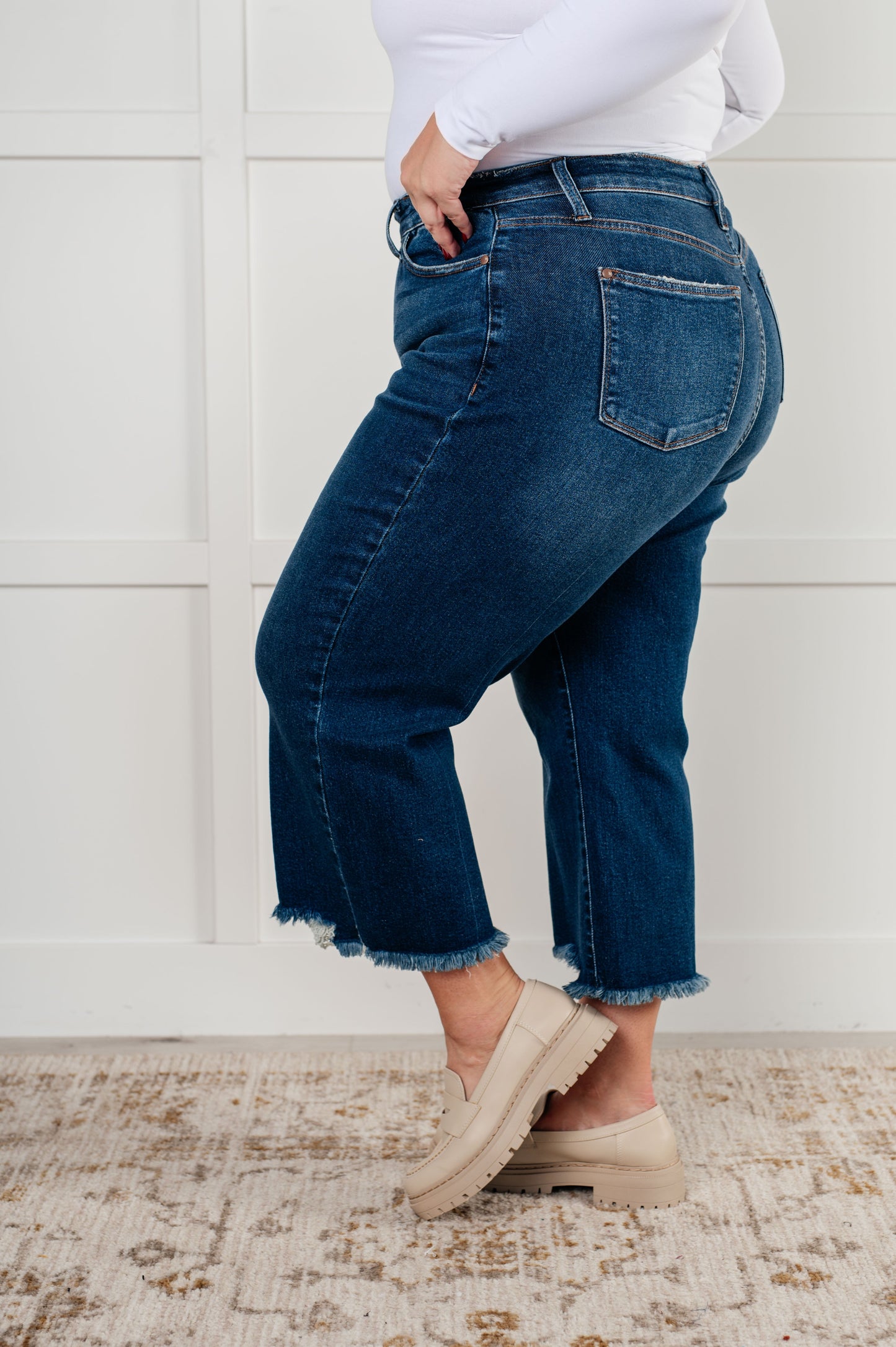 Plus size side view of the Janice High Rise Button Fly Wide Leg Crop Jeans by Judy Blue in a dark wash. Features a high-rise waist, button fly closure, wide leg crop silhouette, raw hem, and 4-way stretch for comfort and style. Perfect for a playful yet sophisticated look.