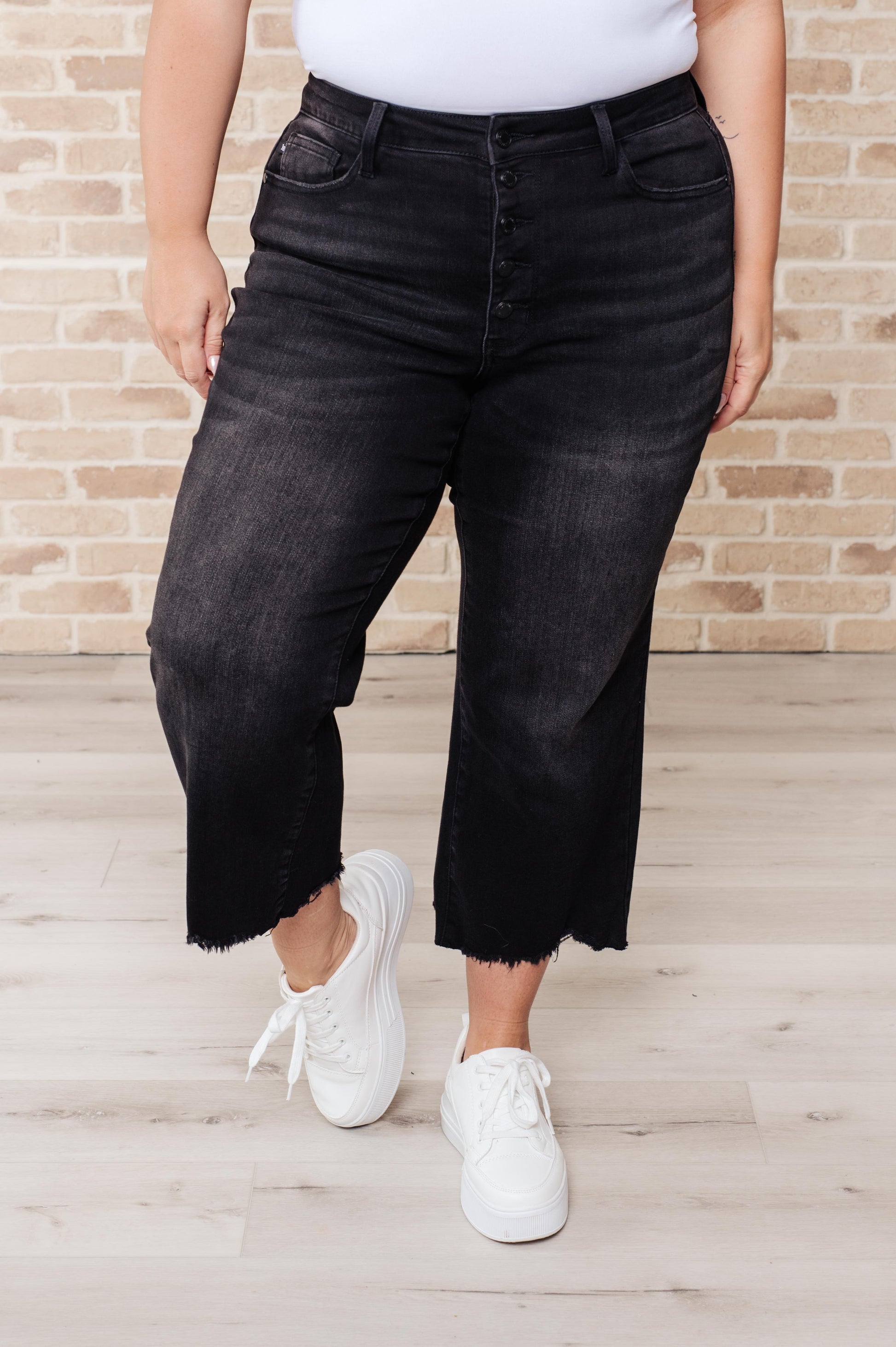 Black garment dyed wide leg crop jeans with high rise, raw hem, and button fly closure.