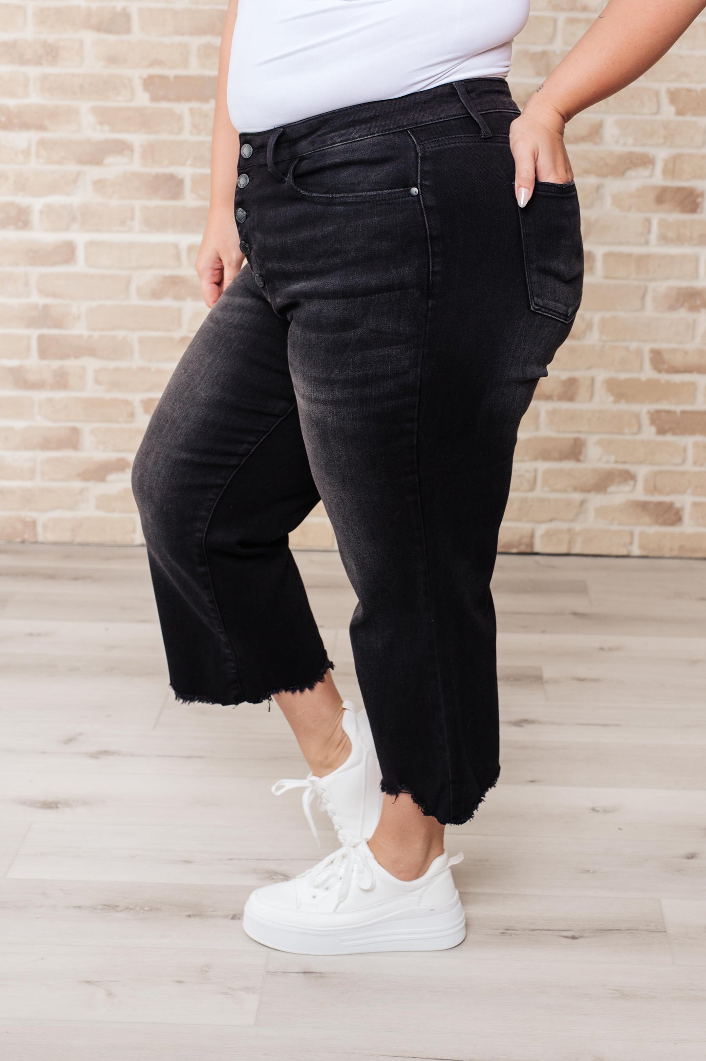 Black garment dyed wide leg crop jeans with high rise, raw hem, and button fly closure.