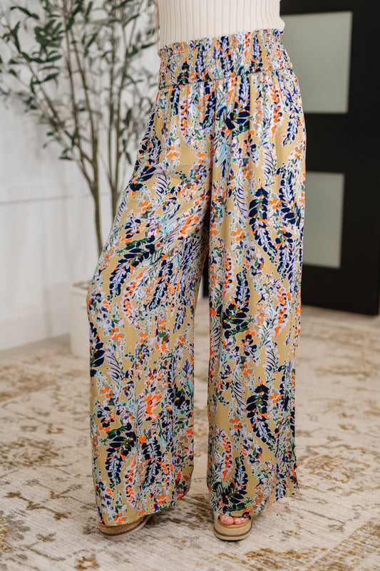 Woman wearing beige floral wide leg pants with smocked waistband and ruffle detail, front view.