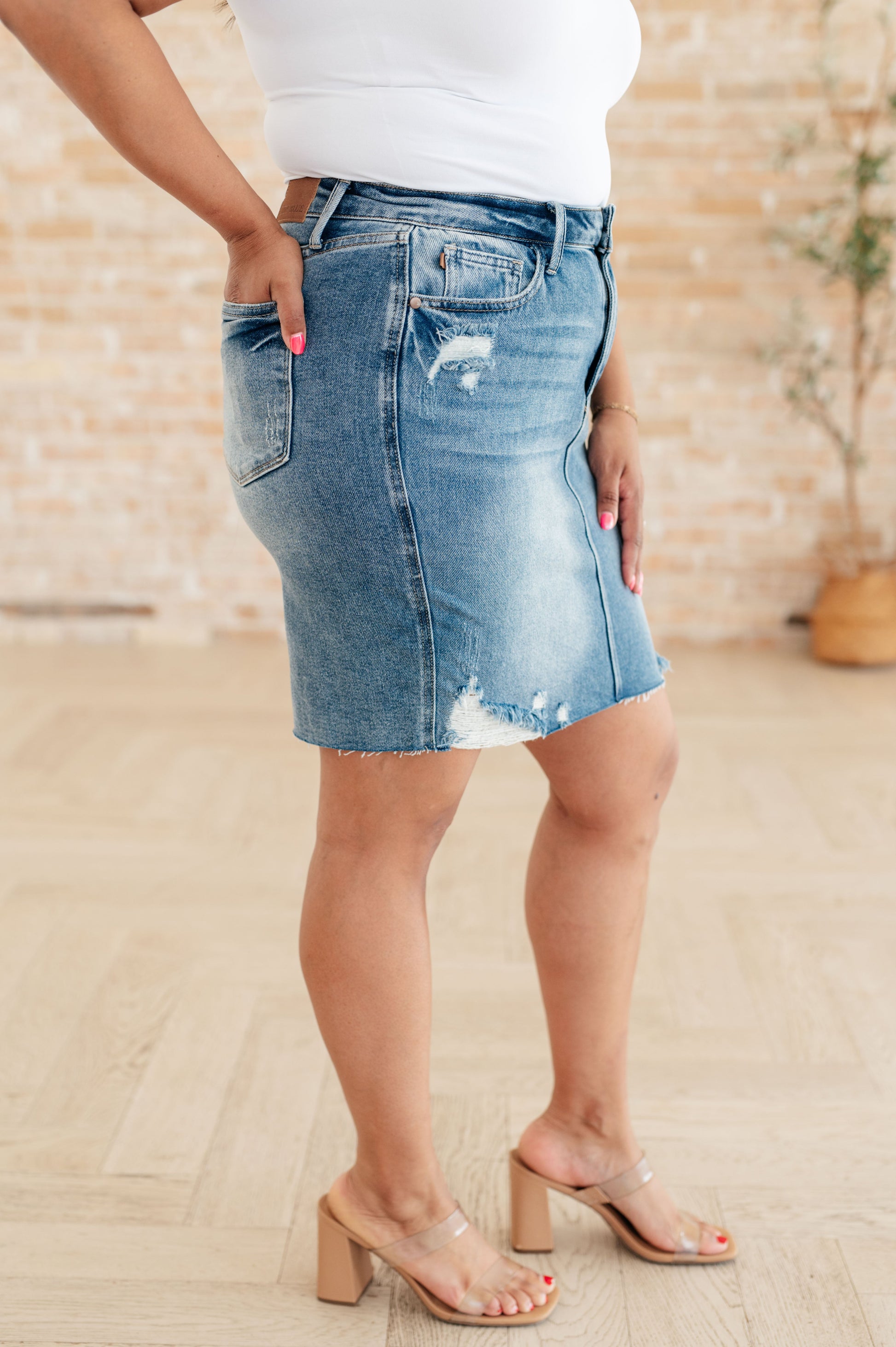 High-rise denim skirt with distressed details and raw hem. Light blue wash, zip fly closure, and a rigid front panel with a stretchy back panel for comfort.