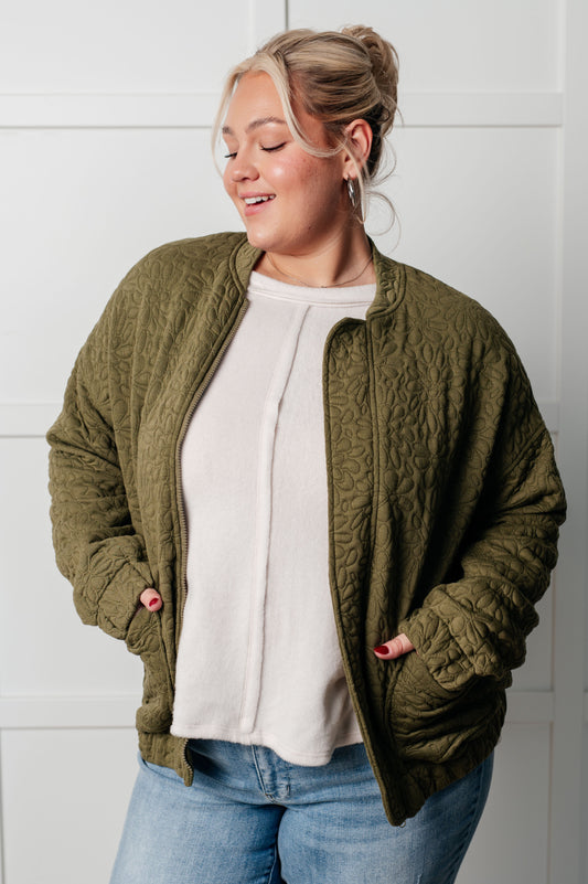 Image of a plus size woman in a green  quilted zip up jacket with a standing collar, quilted knit design, drop shoulders, full zipper, patch pockets, elastic hemline, and sleeve cuffs.