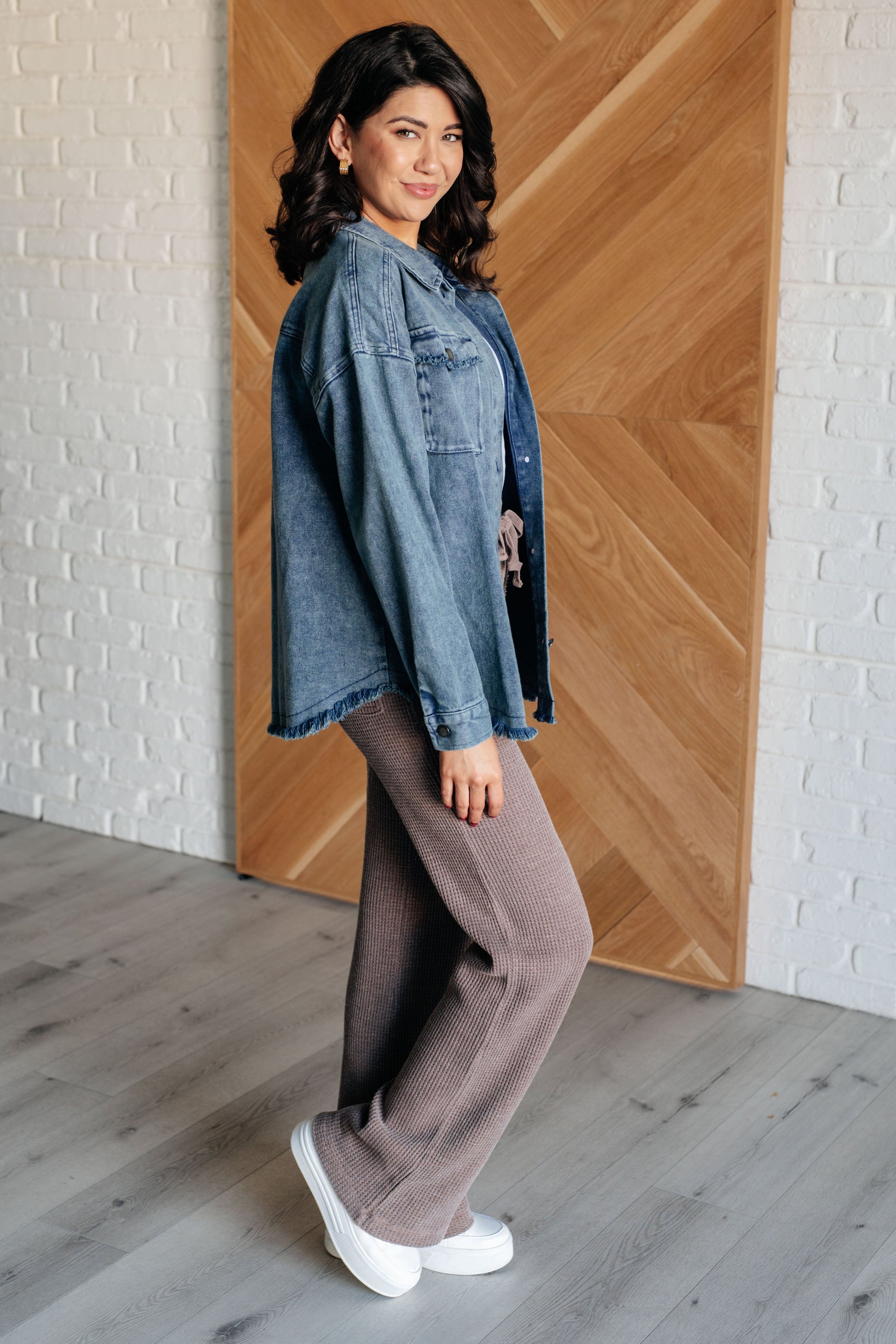 Dark wash mineral-wash denim shacket with a collared neckline, dropped shoulders, and long sleeves. Features a button front, gusseted pocket, raw edge details, back pleat, and raw hem with stay stitching.