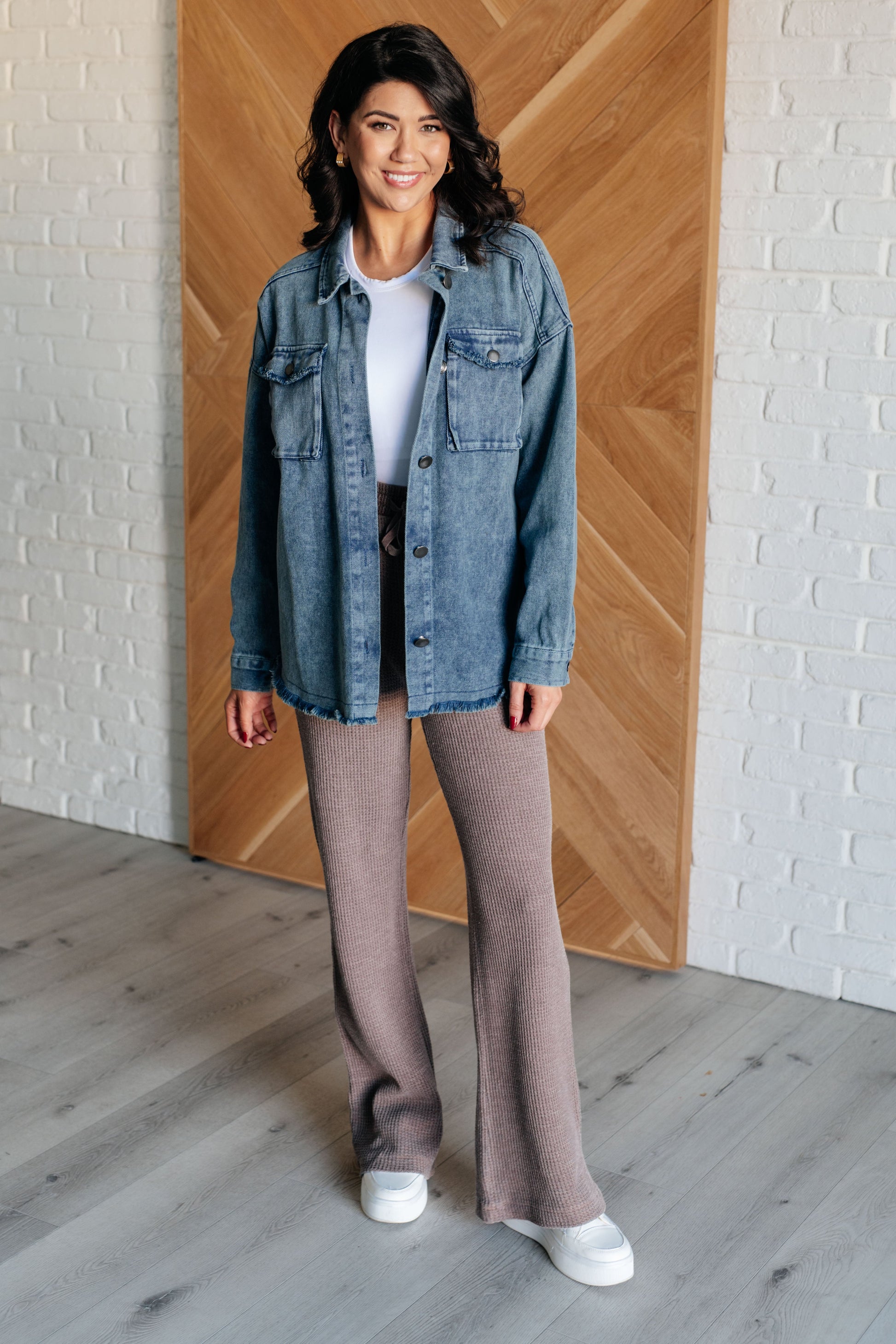 Dark wash mineral-wash denim shacket with a collared neckline, dropped shoulders, and long sleeves. Features a button front, gusseted pocket, raw edge details, back pleat, and raw hem with stay stitching.