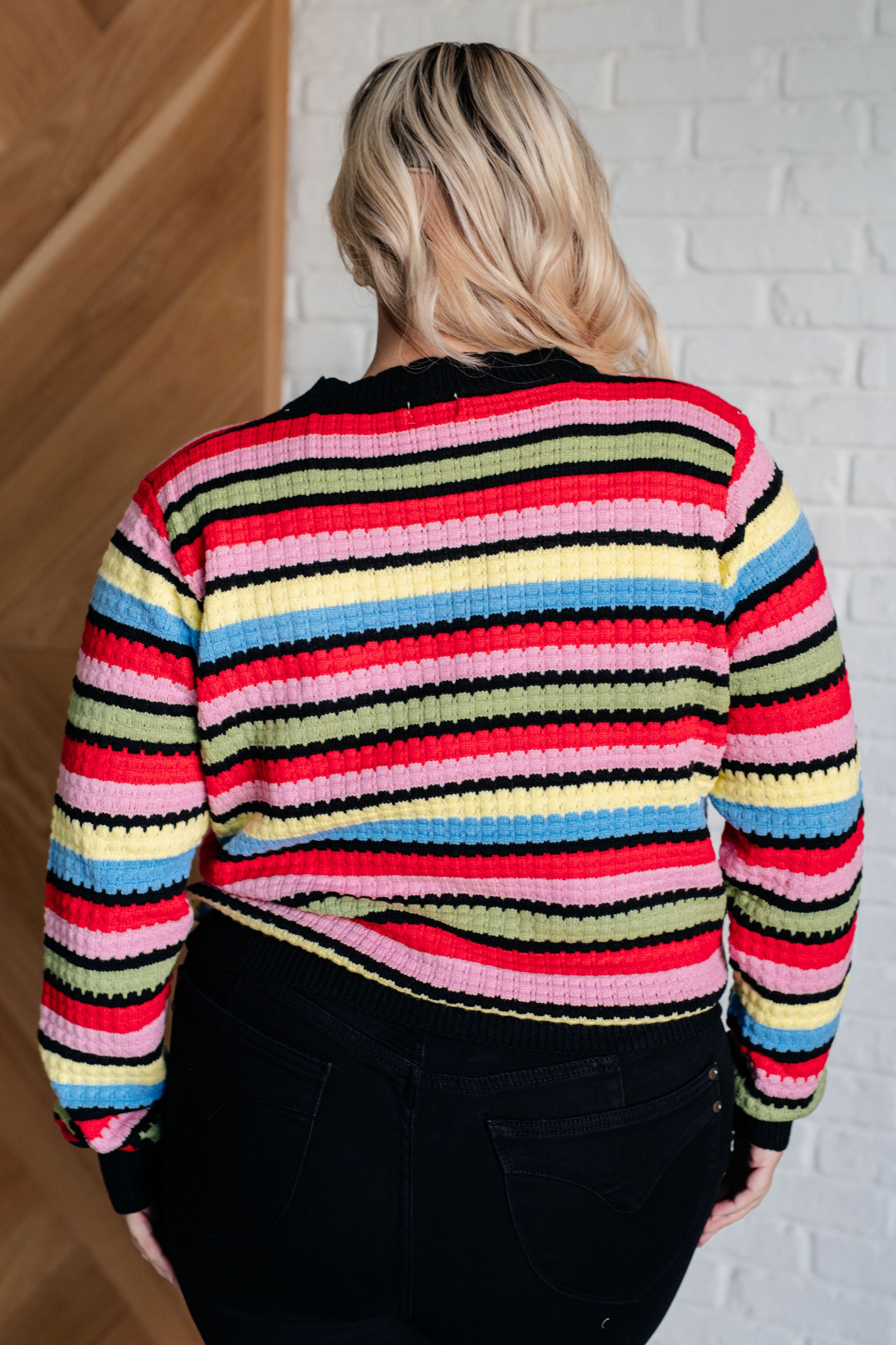 A women's striped sweater made of textured mid-weight knit fabric, featuring a crew neckline, long sleeves, and a comfortable fit. stripes of red, pink, blue, green, black, and yellow.