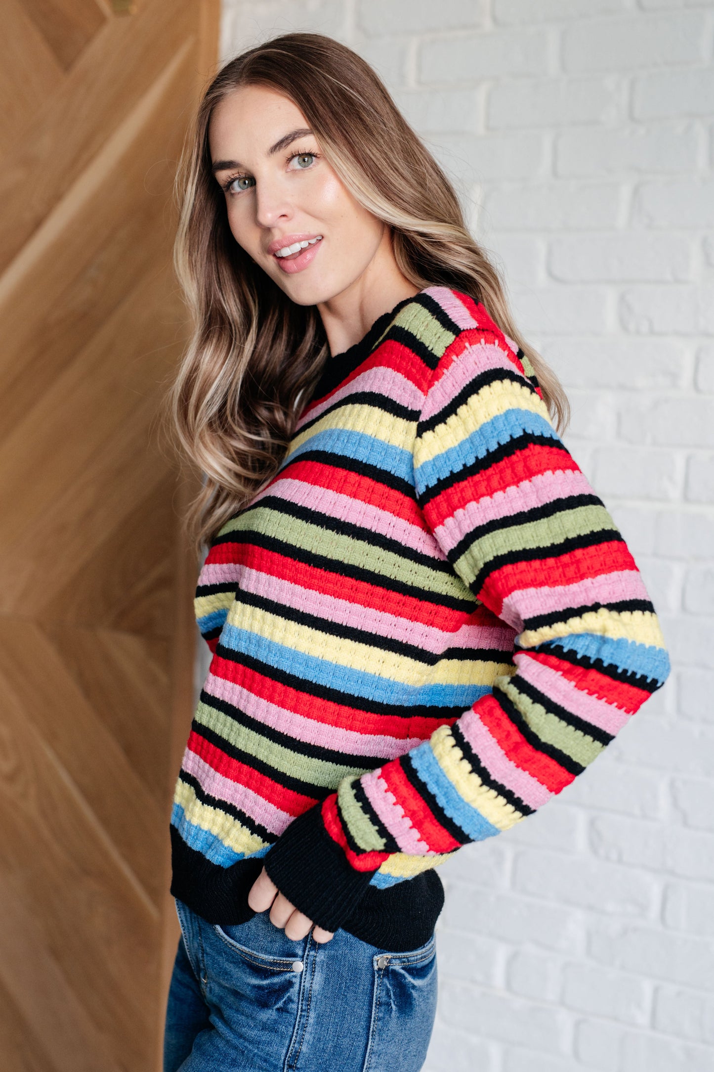 A women's striped sweater made of textured mid-weight knit fabric, featuring a crew neckline, long sleeves, and a comfortable fit. stripes of red, pink, blue, green, black, and yellow.