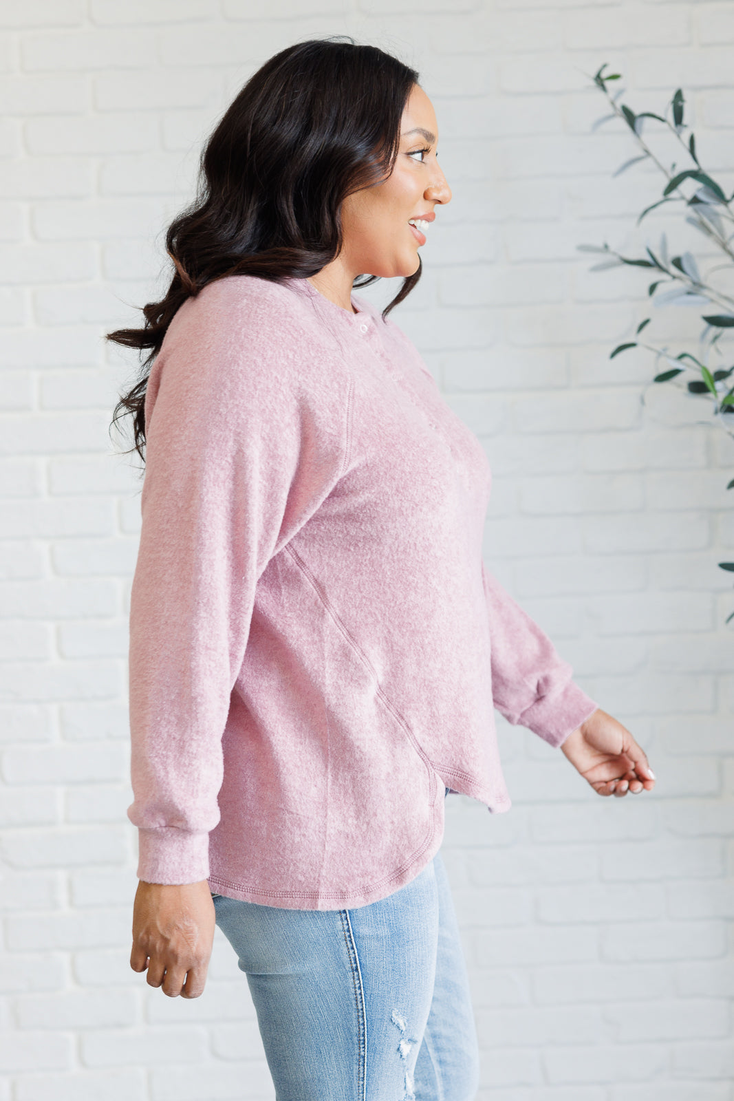 Light rose long-sleeve tee made from soft melange hacci knit fabric. Features a round neckline with half-snap buttons, raglan sleeves, and banded cuffs.