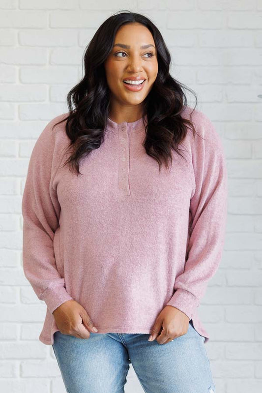 Light rose long-sleeve tee made from soft melange hacci knit fabric. Features a round neckline with half-snap buttons, raglan sleeves, and banded cuffs.