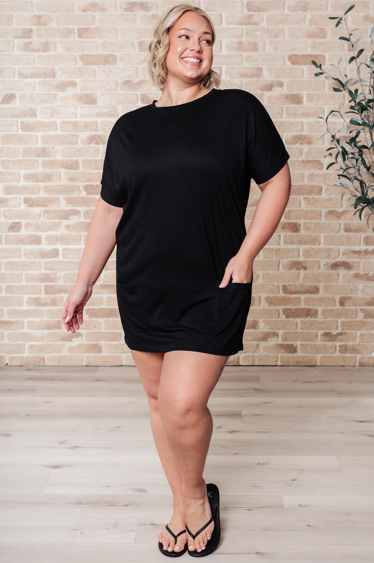 Black pocket tunic dress with a round neckline, short dolman sleeves, and functional patch pockets. Made from lightweight jersey knit.