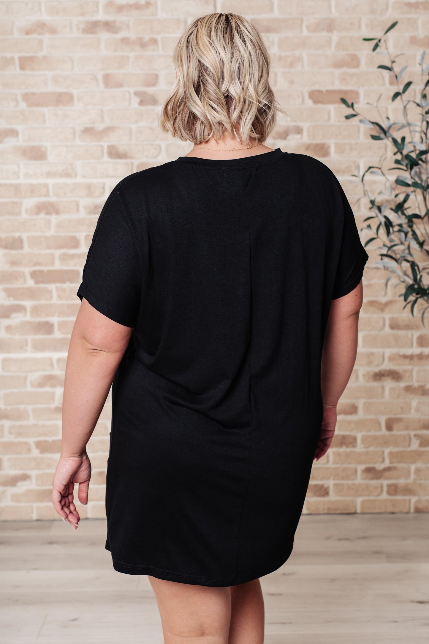 Black pocket tunic dress with a round neckline, short dolman sleeves, and functional patch pockets. Made from lightweight jersey knit.