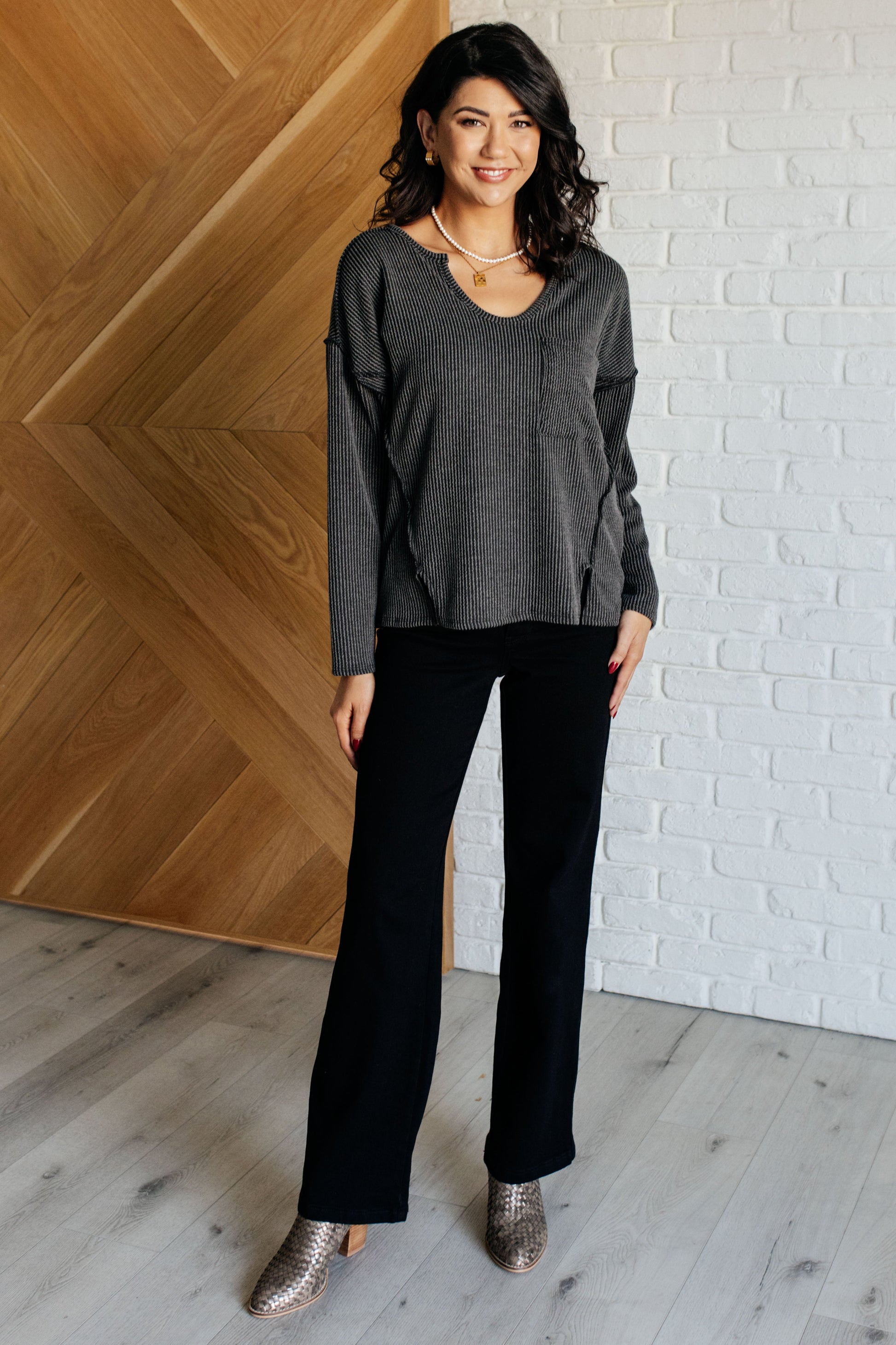 A women's ribbed knit top in charcoal, featuring a notch neckline, long drop-shoulder sleeves, a functional patch pocket, exposed seam details, and front slits.