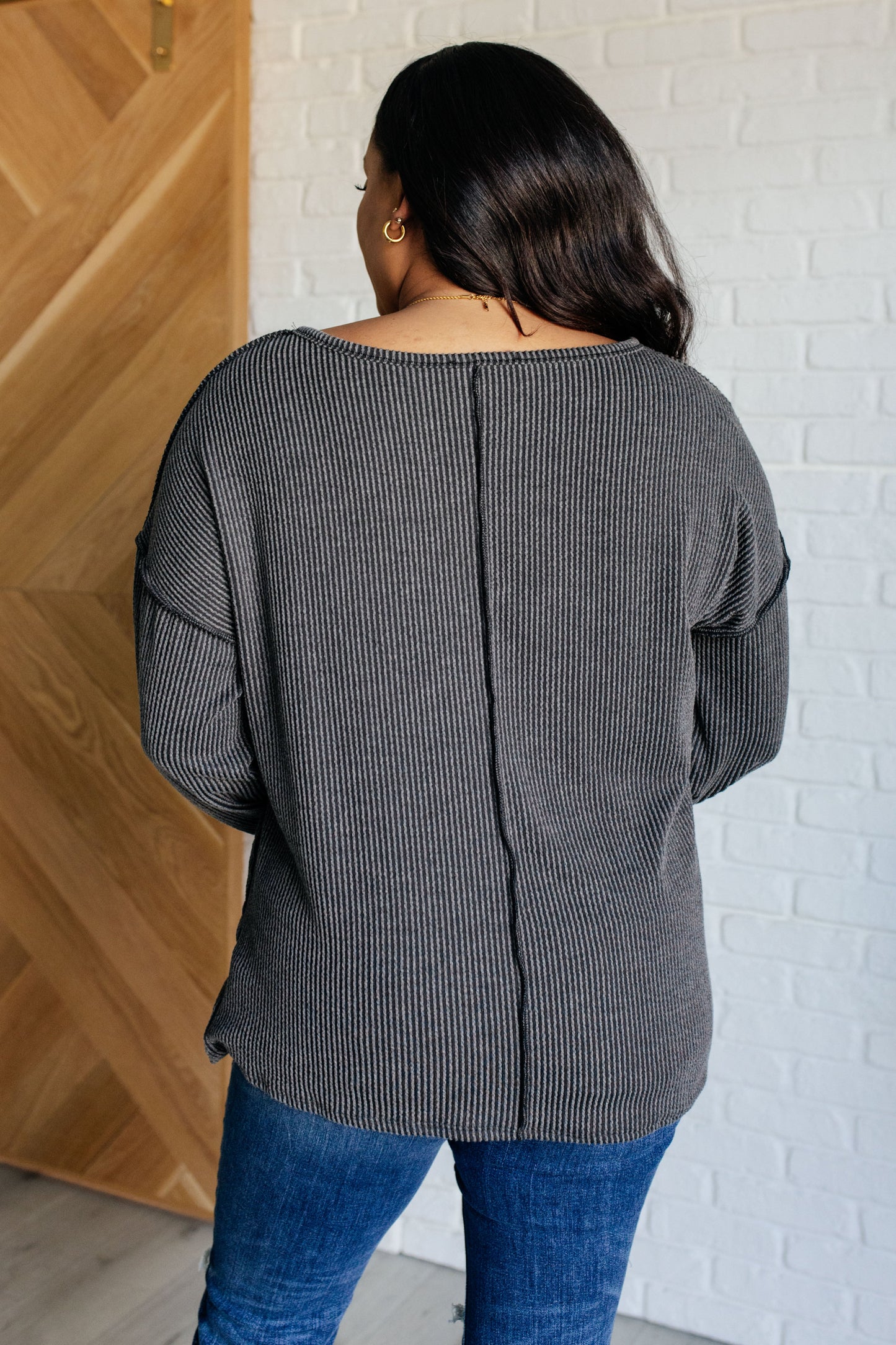 A women's ribbed knit top in charcoal, featuring a notch neckline, long drop-shoulder sleeves, a functional patch pocket, exposed seam details, and front slits.