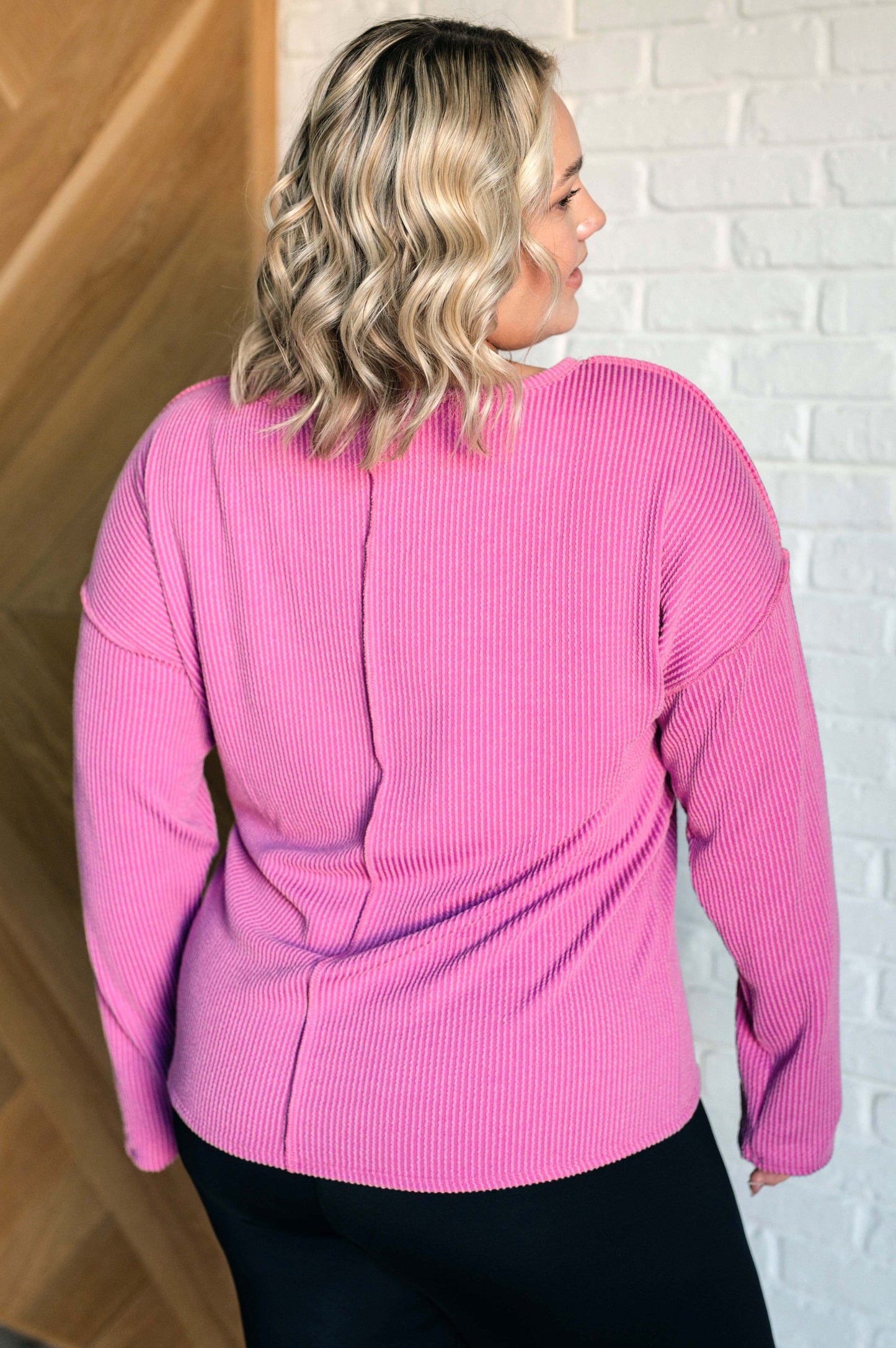 A women's ribbed knit top in magenta, featuring a notch neckline, long drop-shoulder sleeves, a functional patch pocket, exposed seam details, and front slits.