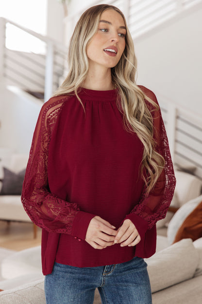 Model wearing Lacey Blouse in wine with mock neckline and long lace sleeves.