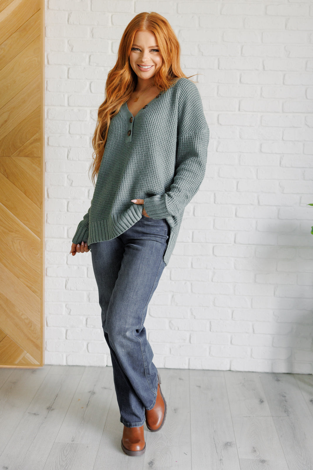 Women's sage waffle knit sweater with long sleeves, a banded ribbed V-neckline, exaggerated ribbed hemline and cuffs, side slits, and functional and faux button closures.