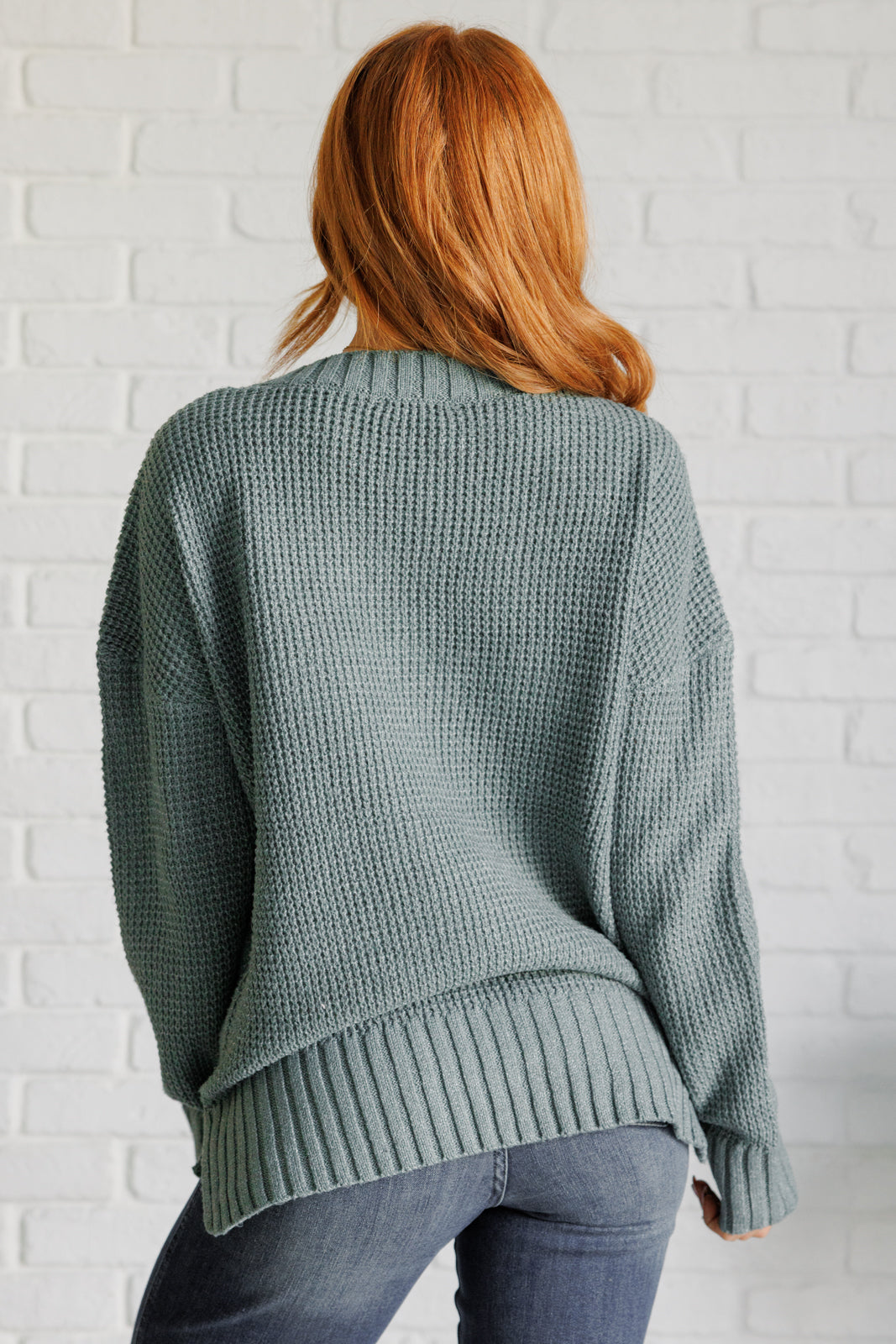 Women's sage waffle knit sweater with long sleeves, a banded ribbed V-neckline, exaggerated ribbed hemline and cuffs, side slits, and functional and faux button closures.