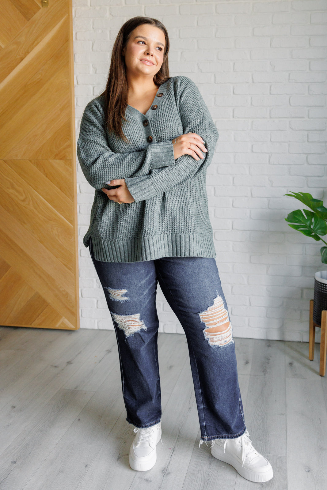 Women's sage waffle knit sweater with long sleeves, a banded ribbed V-neckline, exaggerated ribbed hemline and cuffs, side slits, and functional and faux button closures.