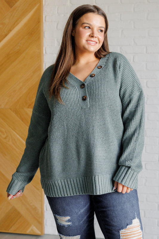 Women's sage waffle knit sweater with long sleeves, a banded ribbed V-neckline, exaggerated ribbed hemline and cuffs, side slits, and functional and faux button closures.