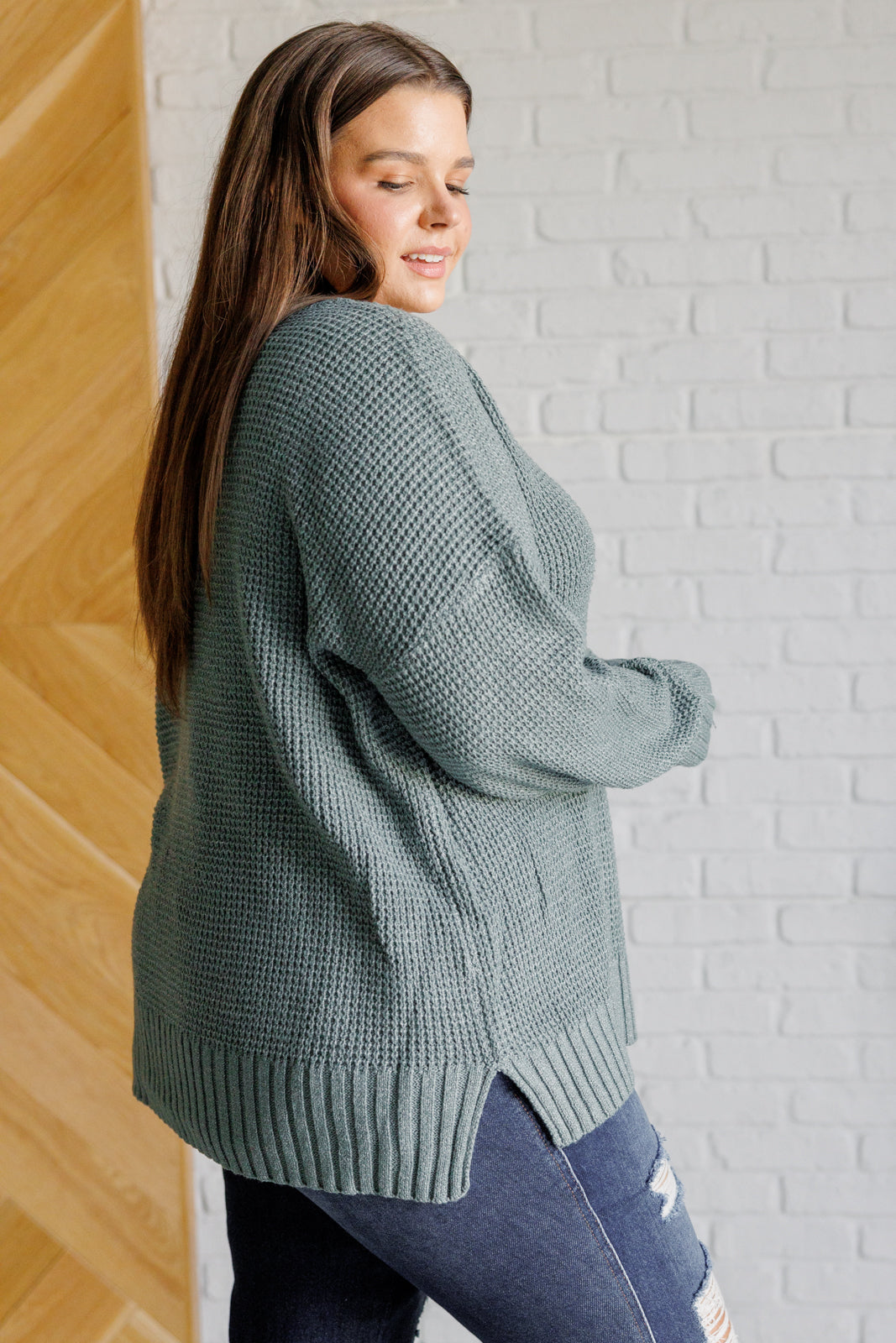 Women's sage waffle knit sweater with long sleeves, a banded ribbed V-neckline, exaggerated ribbed hemline and cuffs, side slits, and functional and faux button closures.