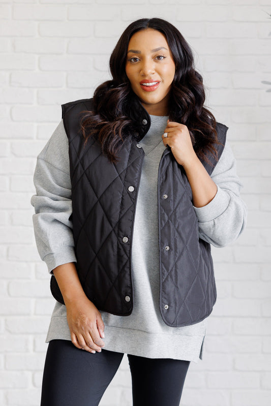 Black puffer vest made from quilted windbreaker material. Features a high neckline, snap button closures, and functional side pockets. Fully lined with a round hemline.