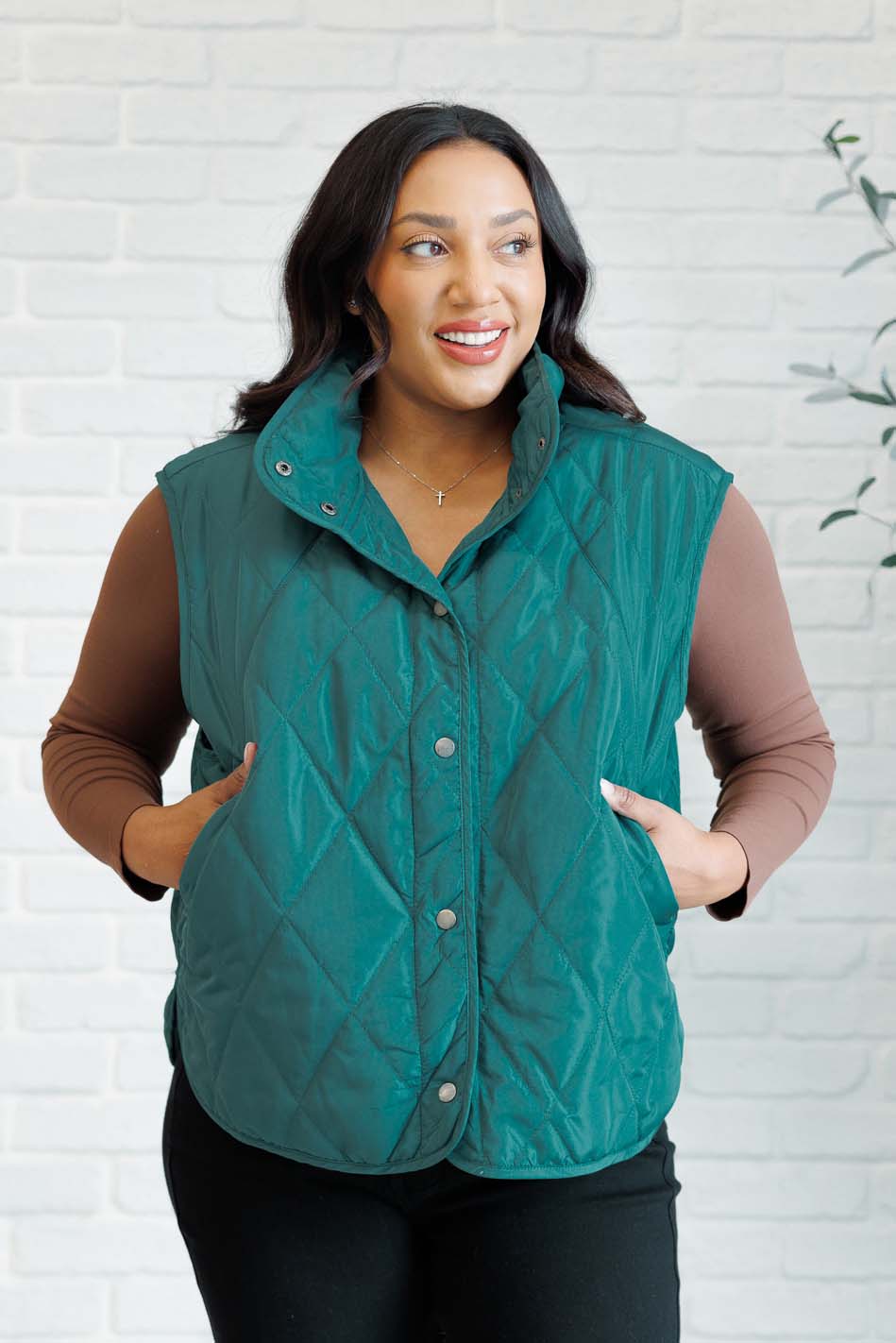 Hunter green puffer vest made from quilted windbreaker material. Features a high neckline, snap button closures, and functional side pockets. Fully lined with a round hemline.