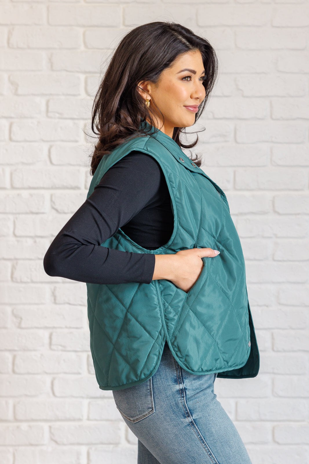 Hunter green puffer vest made from quilted windbreaker material. Features a high neckline, snap button closures, and functional side pockets. Fully lined with a round hemline.