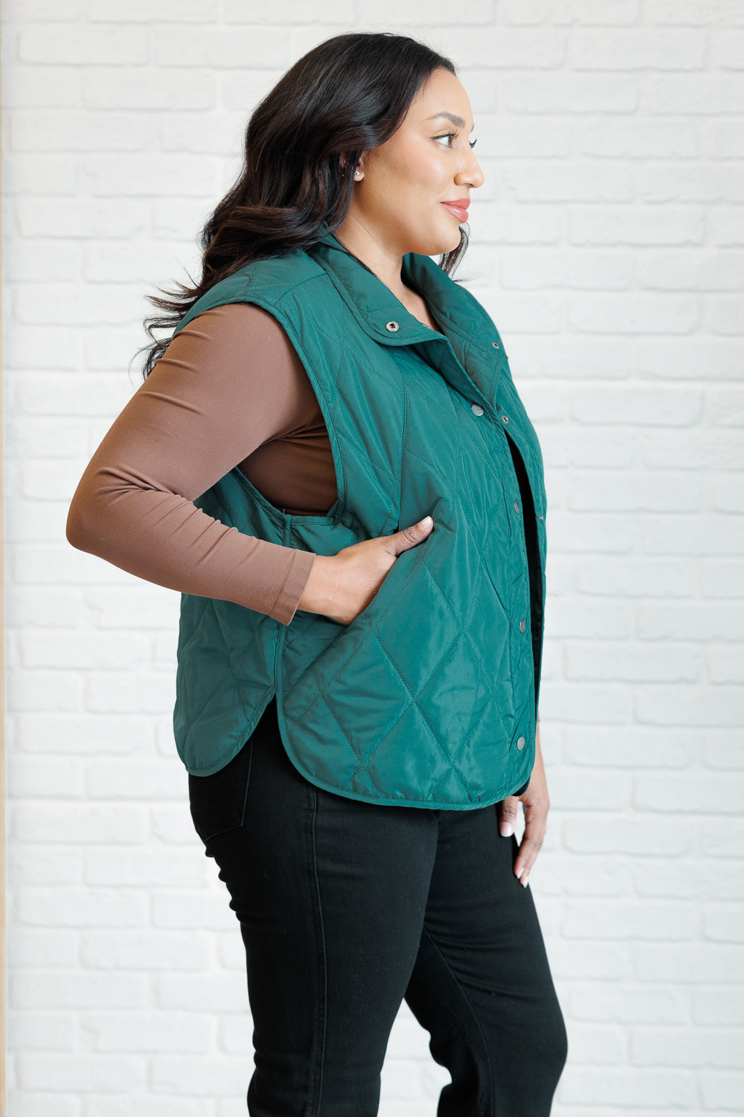 Hunter green puffer vest made from quilted windbreaker material. Features a high neckline, snap button closures, and functional side pockets. Fully lined with a round hemline.