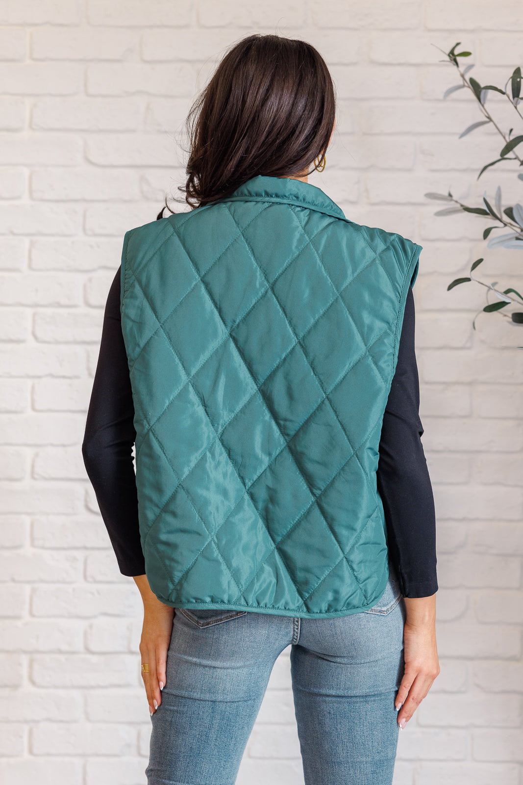 Hunter green puffer vest made from quilted windbreaker material. Features a high neckline, snap button closures, and functional side pockets. Fully lined with a round hemline.