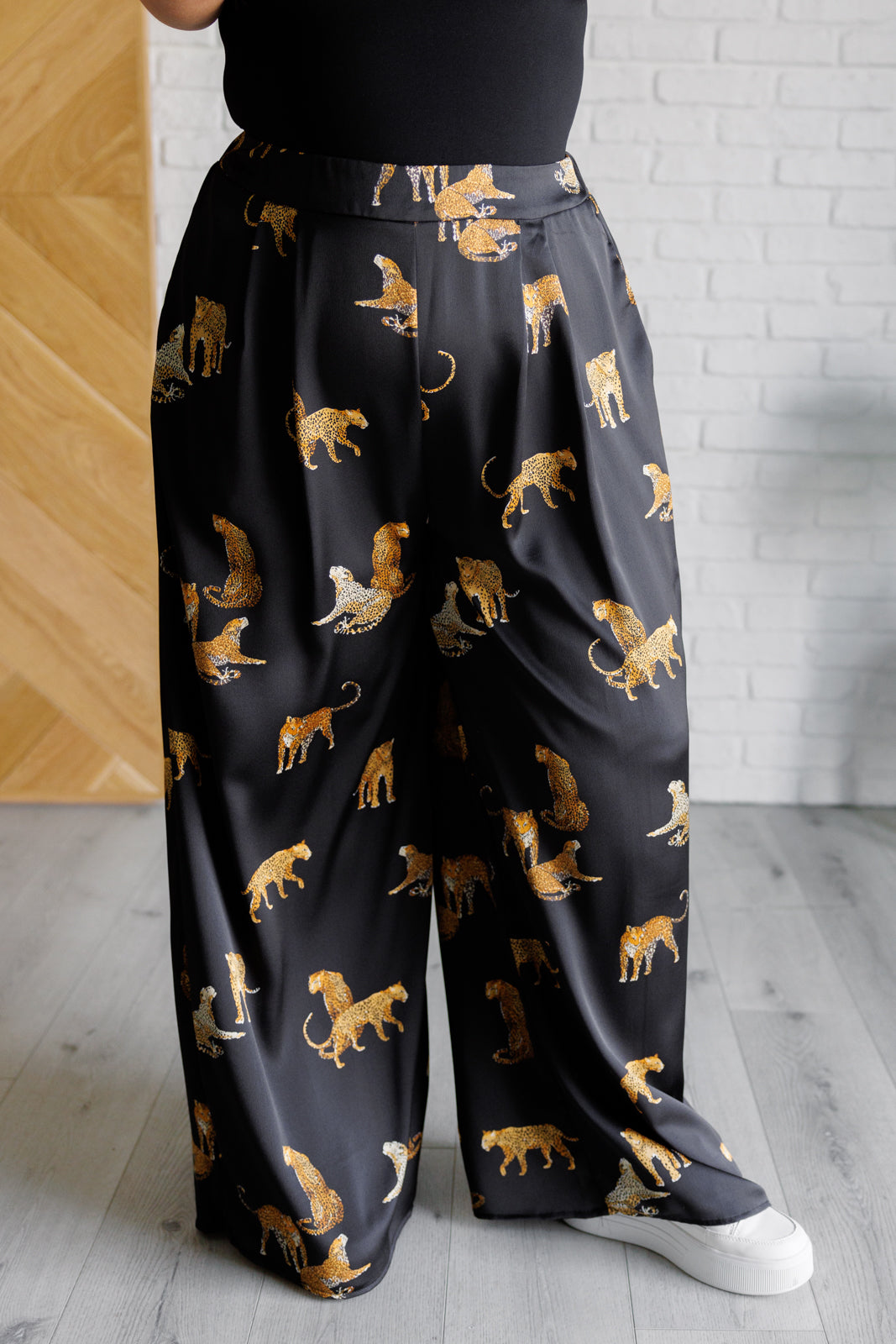 Satin Wide Leg Pants featuring a bold leopard print, high-rise elastic back waistband, and wide-leg silhouette. Made from poly satin with pleat front, pockets, and button-tab closure for a chic and comfortable fit.