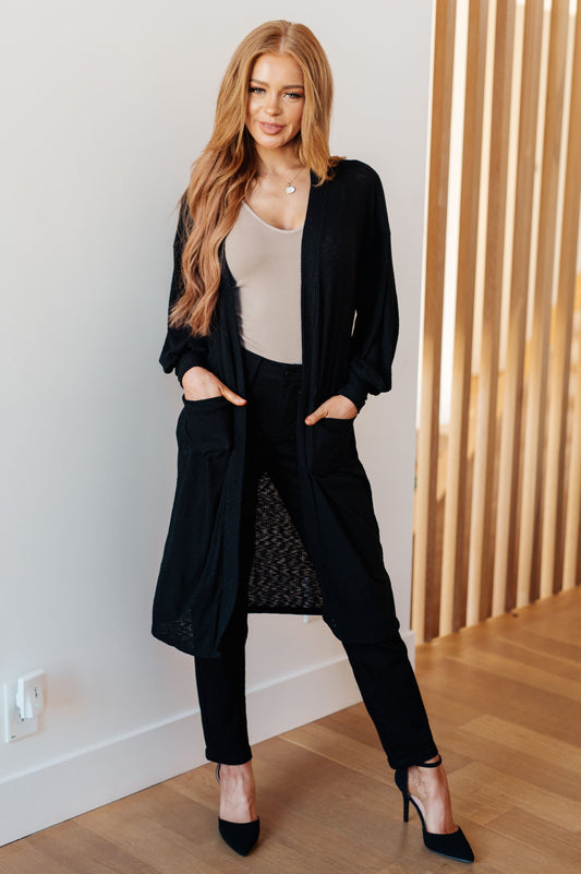 Model wearing Lee Duster Cardigan in Black with long balloon sleeves and patch pockets.