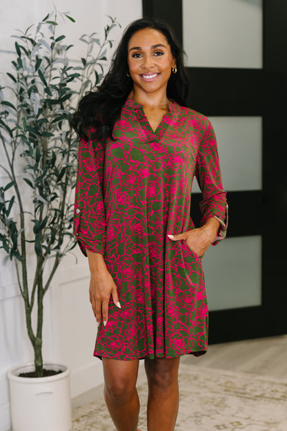 Model wearing Lizzy Long Sleeve Dress in pink and olive floral print with V-neckline and side pockets.