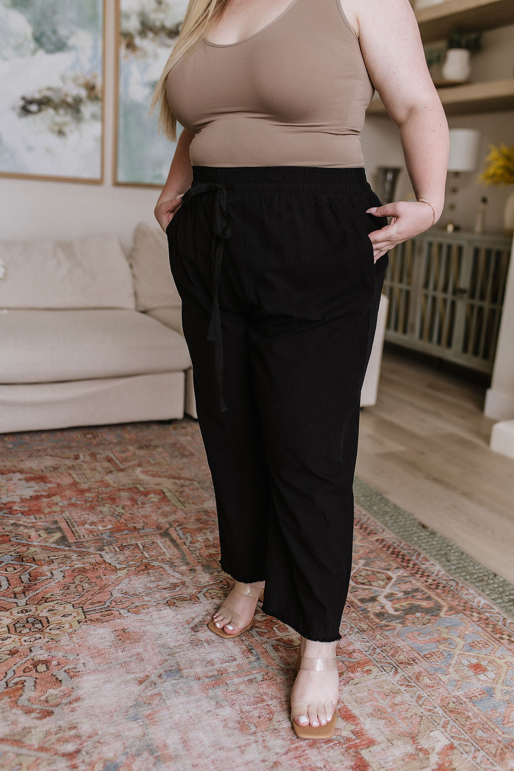 Black high-waisted pants with relaxed fit, raw hem, elastic waistband, and functional drawstring.