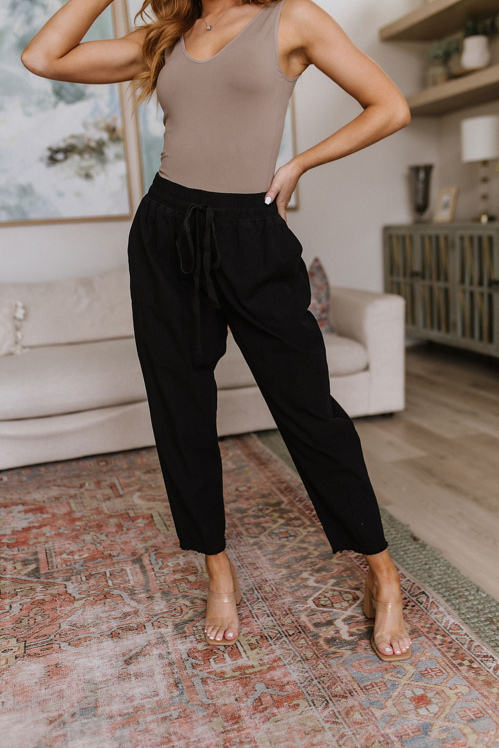 Black high-waisted pants with relaxed fit, raw hem, elastic waistband, and functional drawstring.