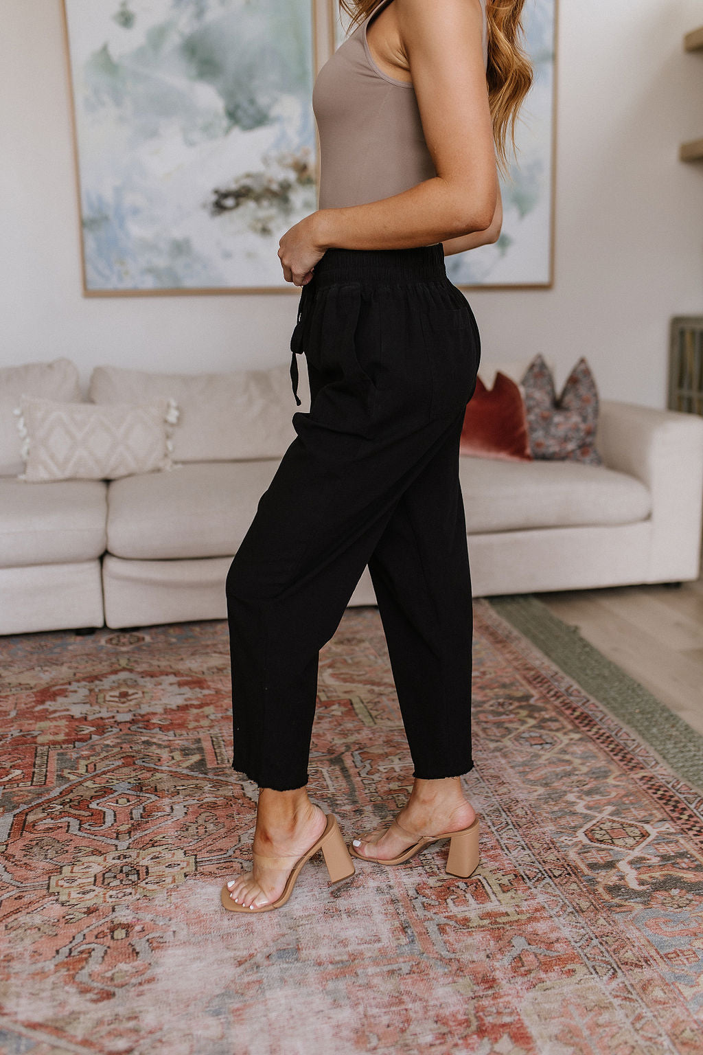 Black high-waisted pants with relaxed fit, raw hem, elastic waistband, and functional drawstring.