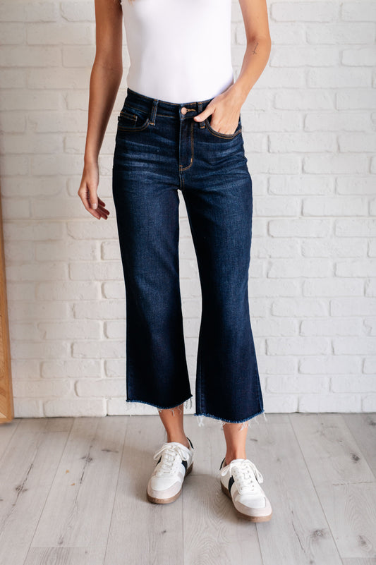 Judy Blue dark wash high-rise cropped wide leg jeans with a raw hem, tummy control technology, and 4-way stretch for comfort. Features a zip fly and control top.